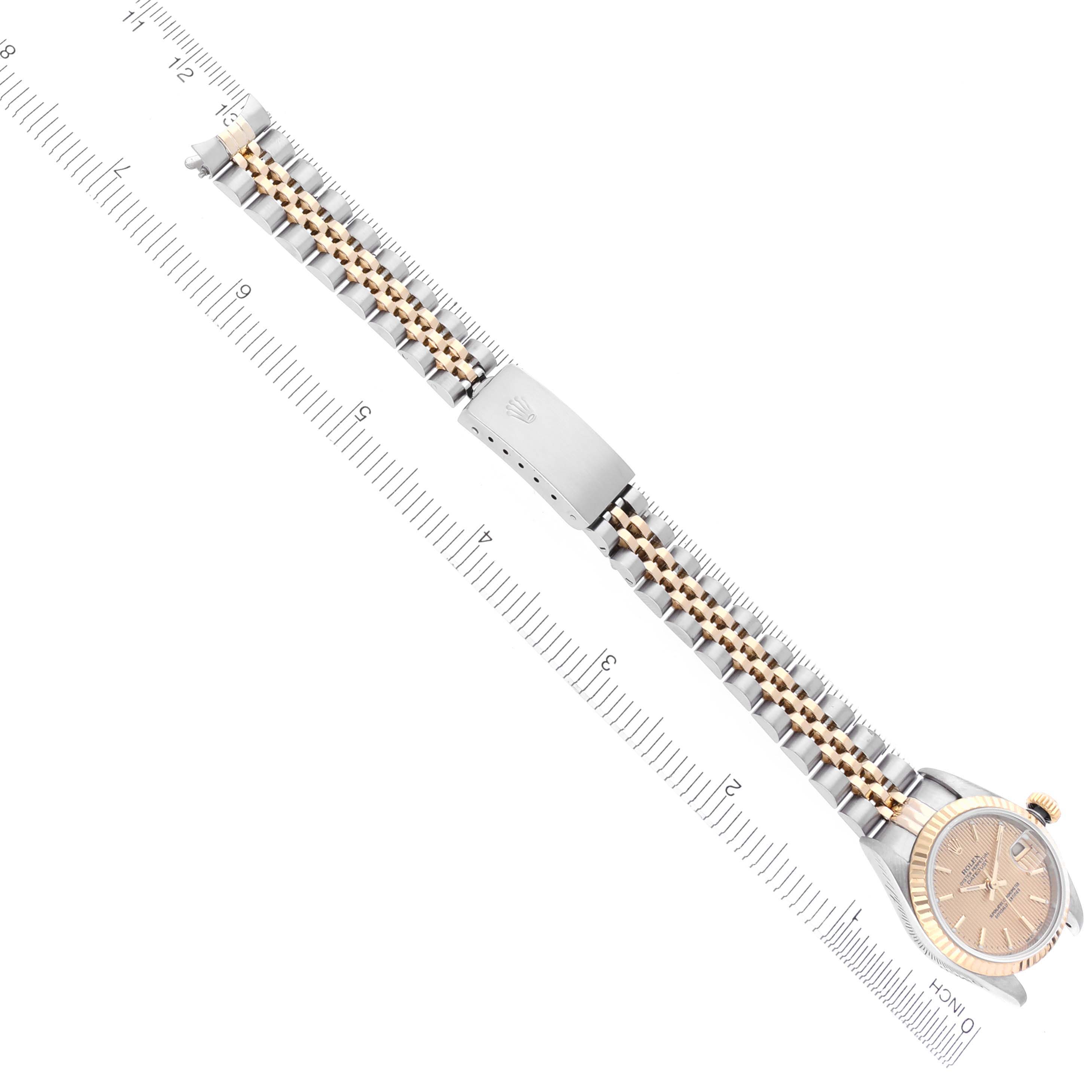 The Rolex Datejust 79173 Women's Steel and Gold (two tone) Champagne Dial 79173 Women's Steel and Gold (two tone) Champagne Dial watch is shown from a top-down angle, highlighting its face, bracelet, and clasp against a ruler for scale.