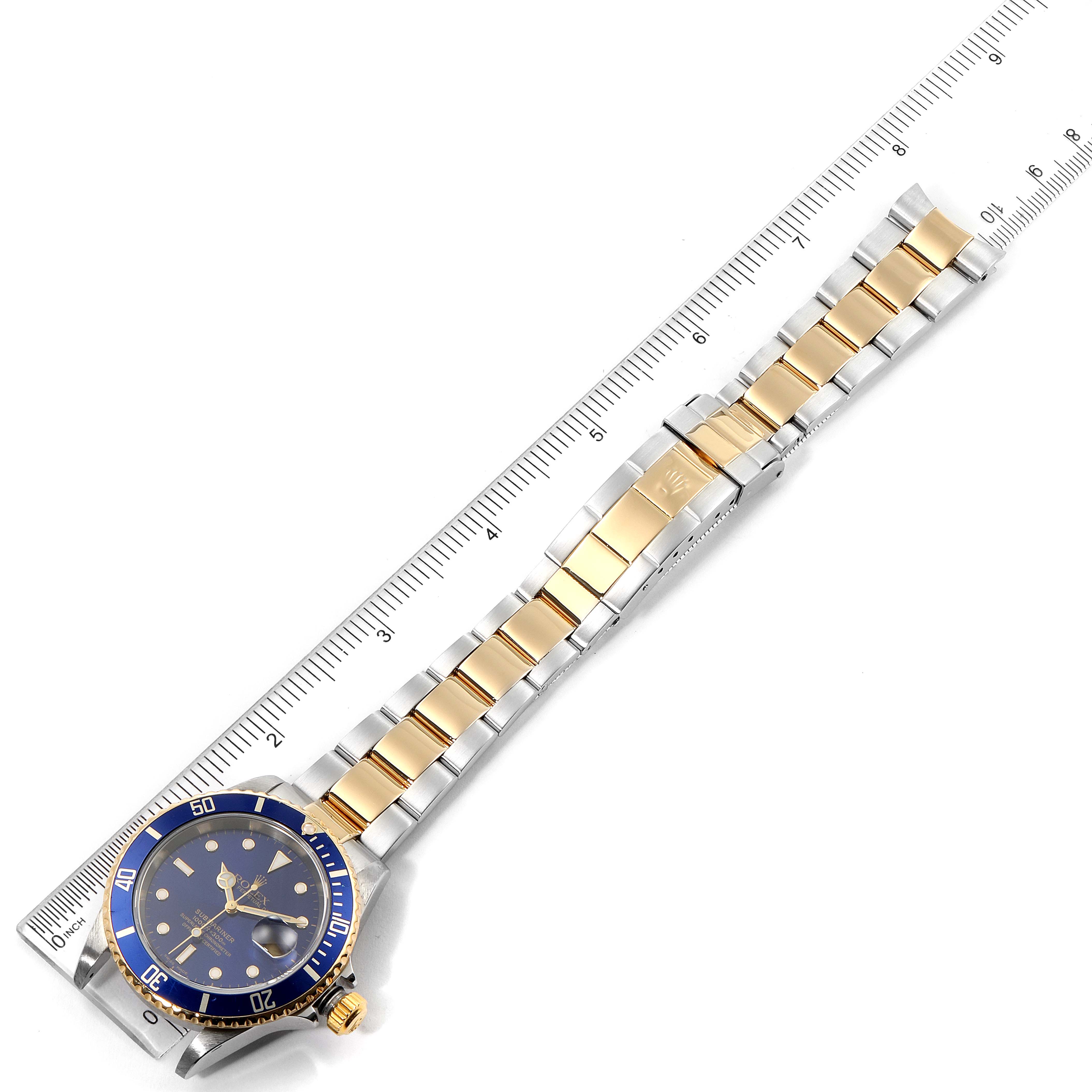 The image shows a Rolex Submariner 16613 Men's Steel and Gold (two tone) Blue Dial 16613 Men's Steel and Gold (two tone) Blue Dial watch at a top-down angle, displaying the dial, bezel, and two-tone bracelet beside a ruler.