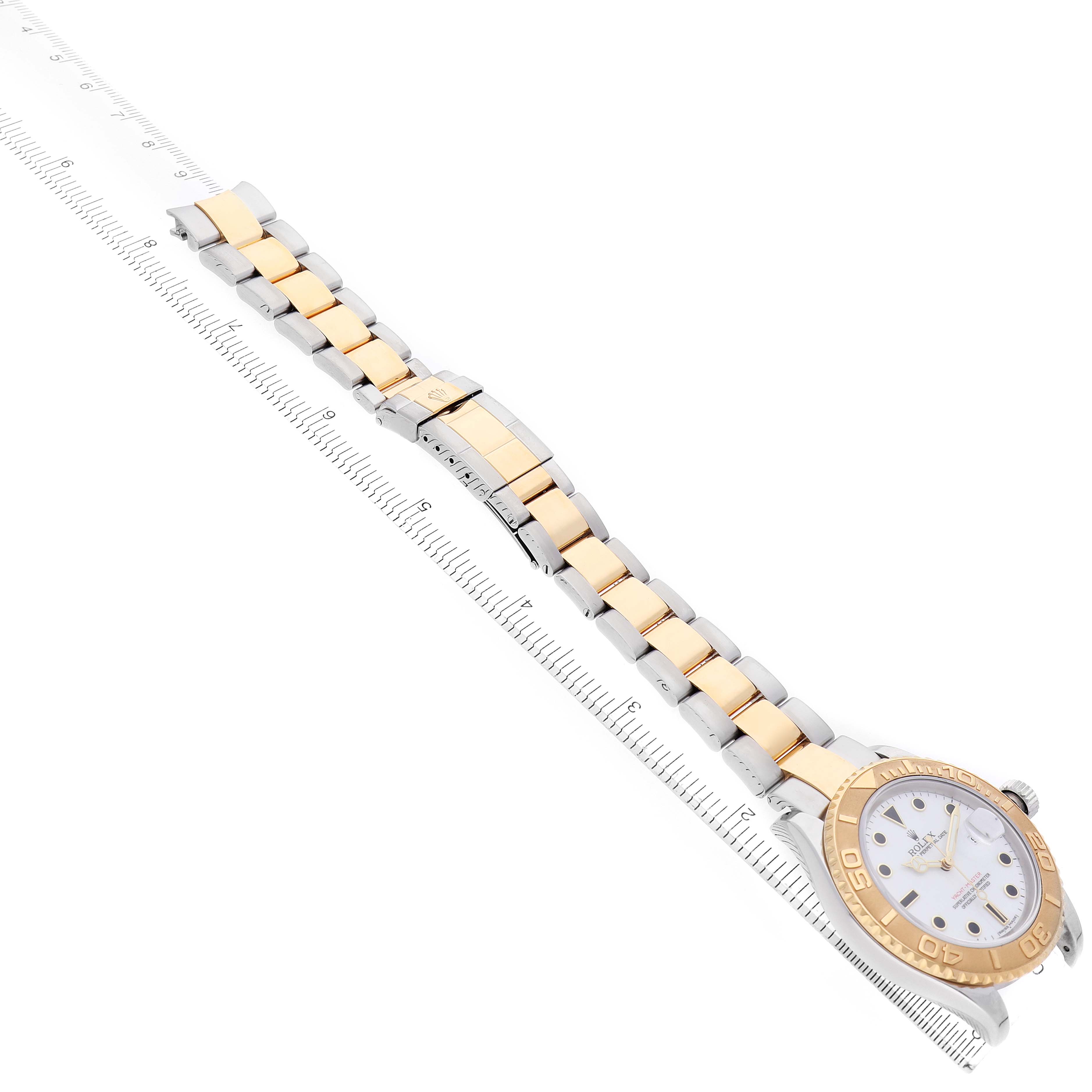 The Rolex Yacht-Master 16623 Men's Steel and Gold (two tone) White Dial watch is shown at an angle displaying its gold and silver bracelet and round face with a ruler beside it.