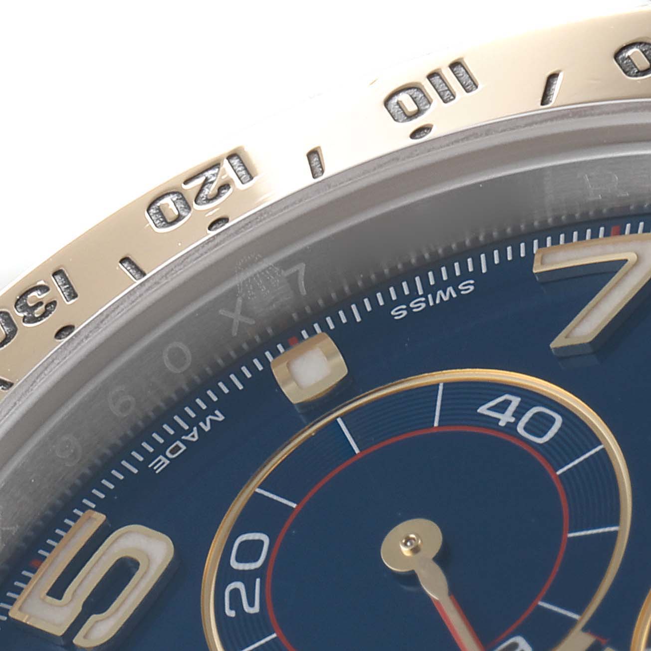 This close-up of a Rolex Daytona 116523 Men
s Steel and Gold (two tone) Blue Dial 116523 Men
s Steel and Gold (two tone) Blue Dial watch shows the bezel, part of the dial, and several numerals.