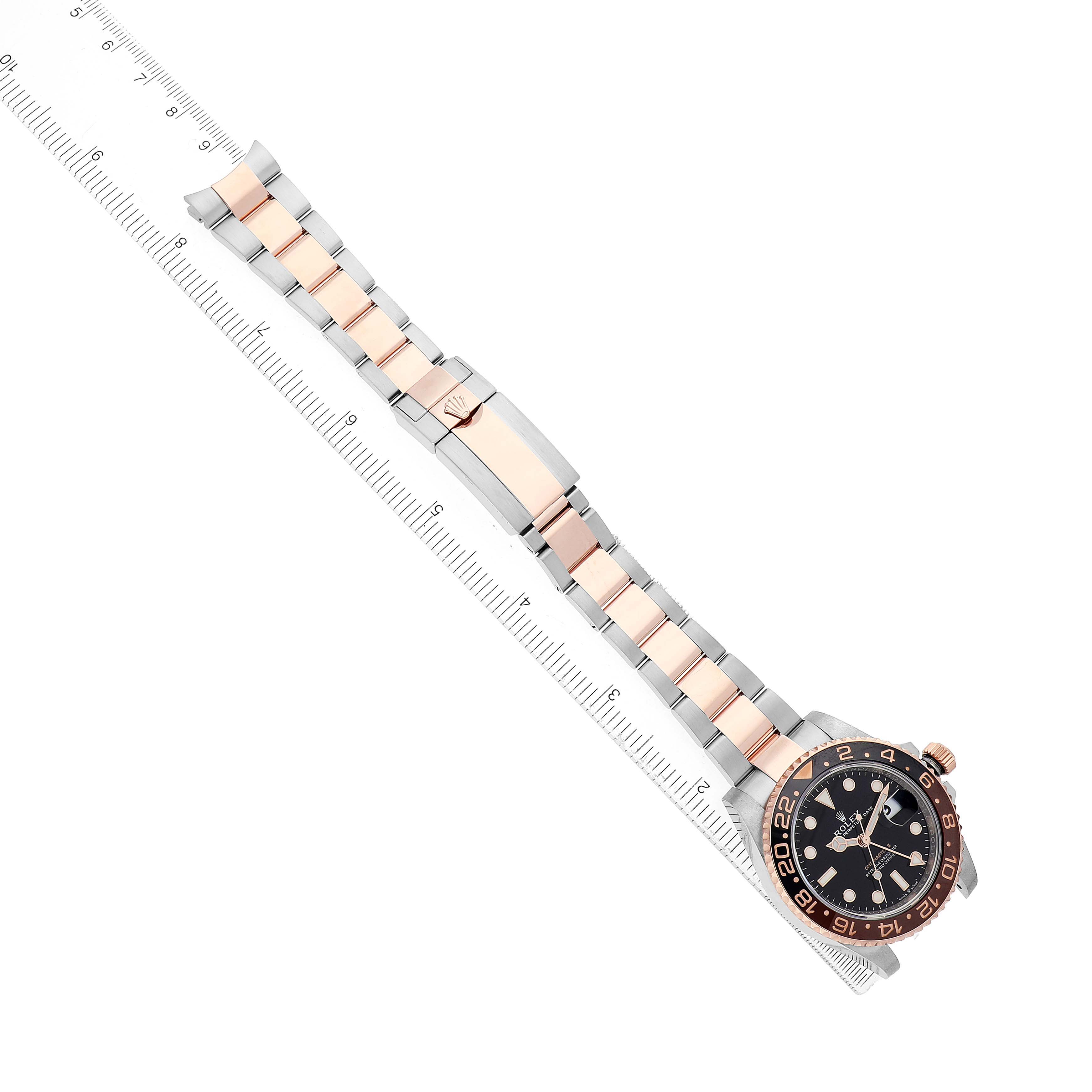 The Rolex GMT-Master 126711 Men's Steel and Gold (two tone) Black Dial watch is shown at an overhead angle, displaying the dial, bezel, and entire bracelet alongside a ruler.
