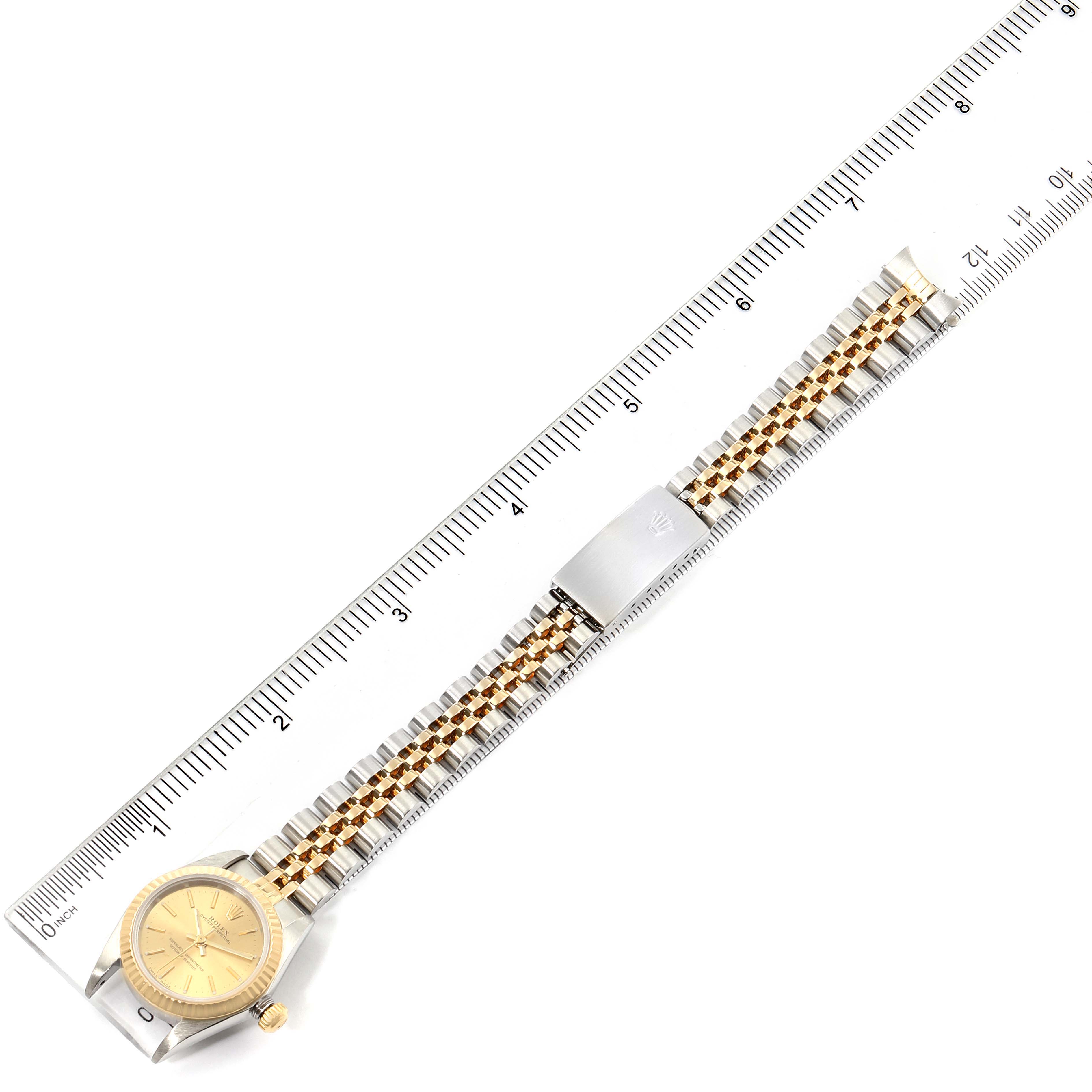 The Rolex Oyster Perpetual 76193 Women
s Steel and Gold (two tone) Champagne Dial 76193 Women
s Steel and Gold (two tone) Champagne Dial watch is shown from a top-down angle, displaying its full band against a ruler for scale.