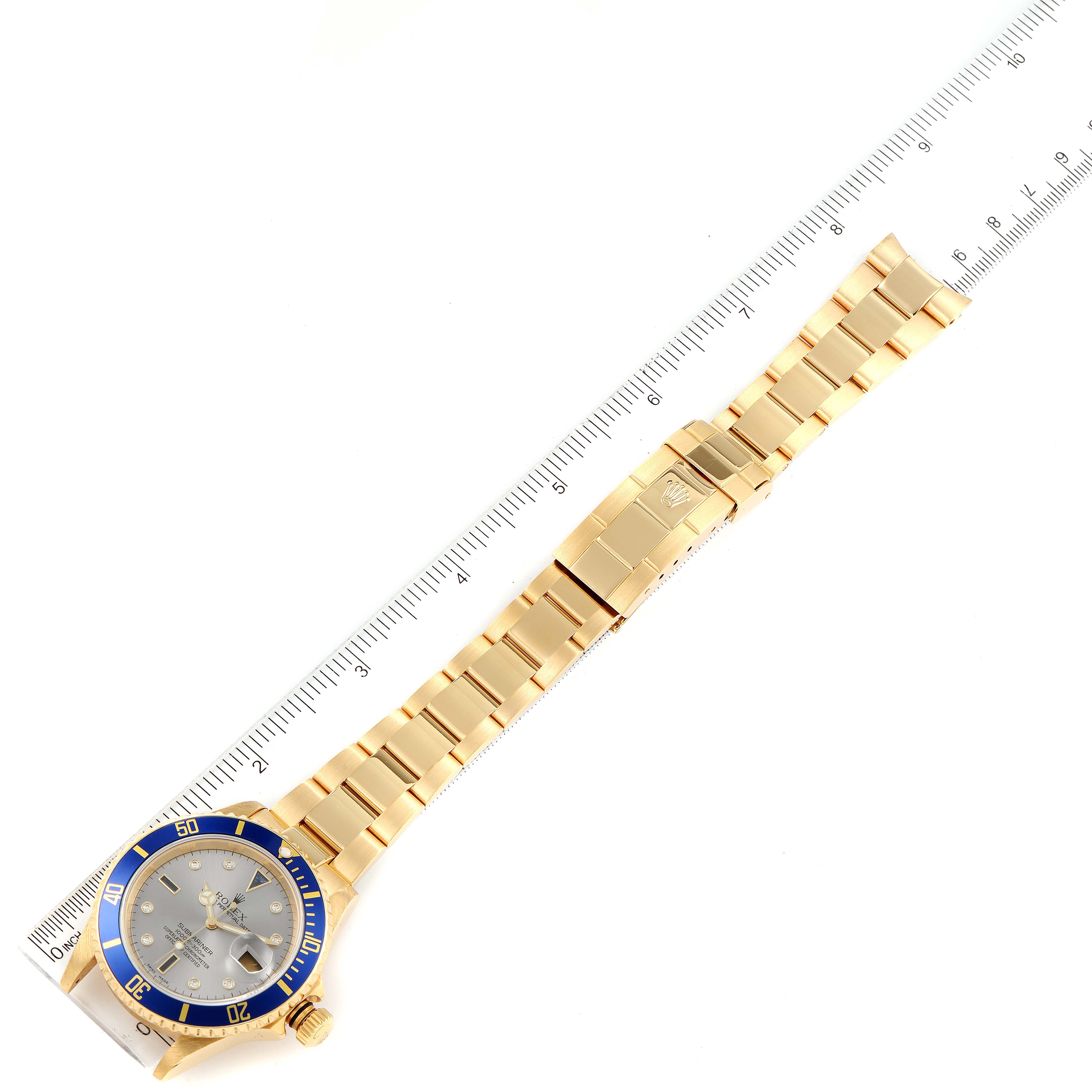 The image shows a top-down view of a Rolex Submariner 16618 Men's Yellow Gold Grey Dial 16618 Men's Yellow Gold Grey Dial watch, highlighting its blue bezel, dial, and gold bracelet against a ruler.