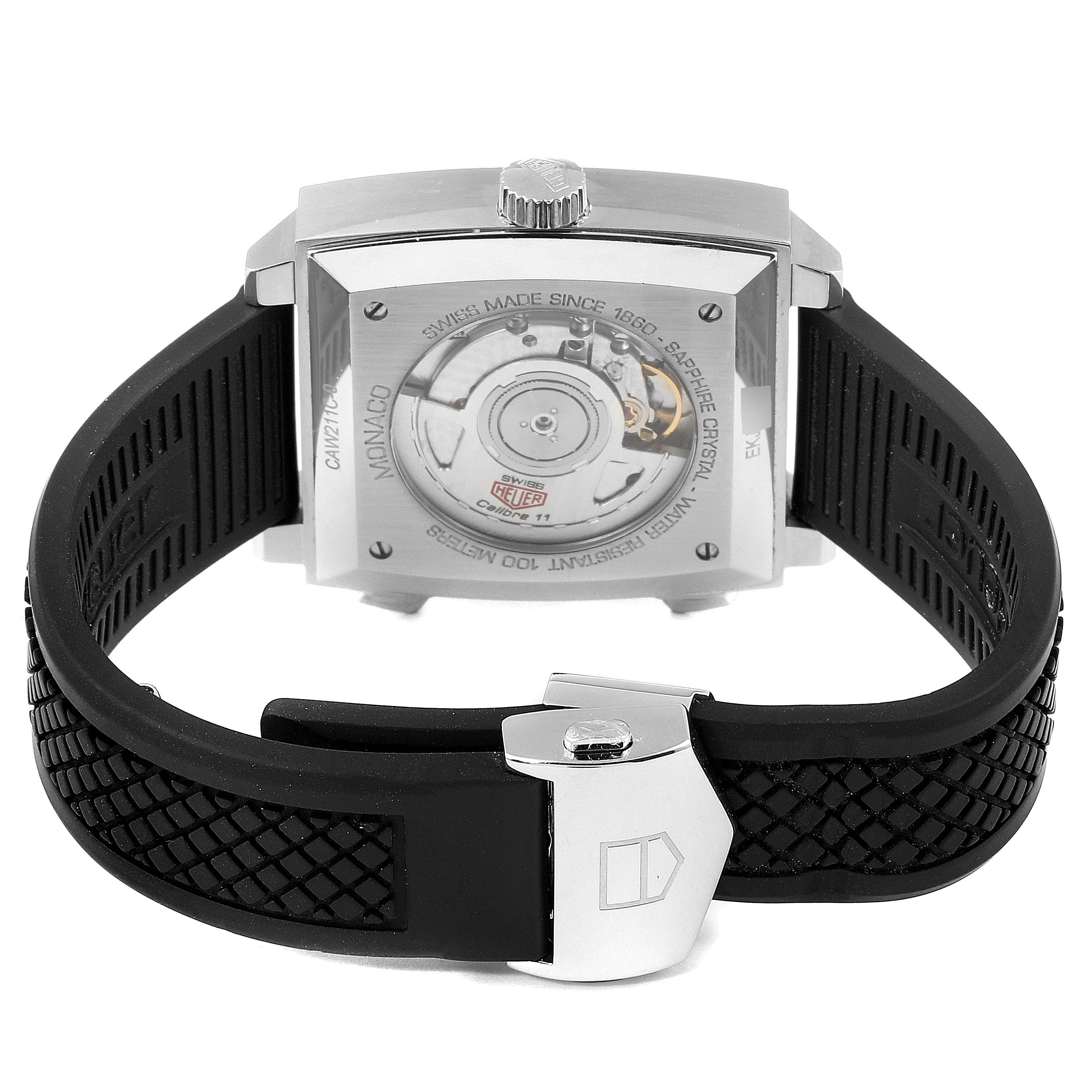 The Tag Heuer Monaco watch is shown from the back, showcasing its movement and black rubber strap.