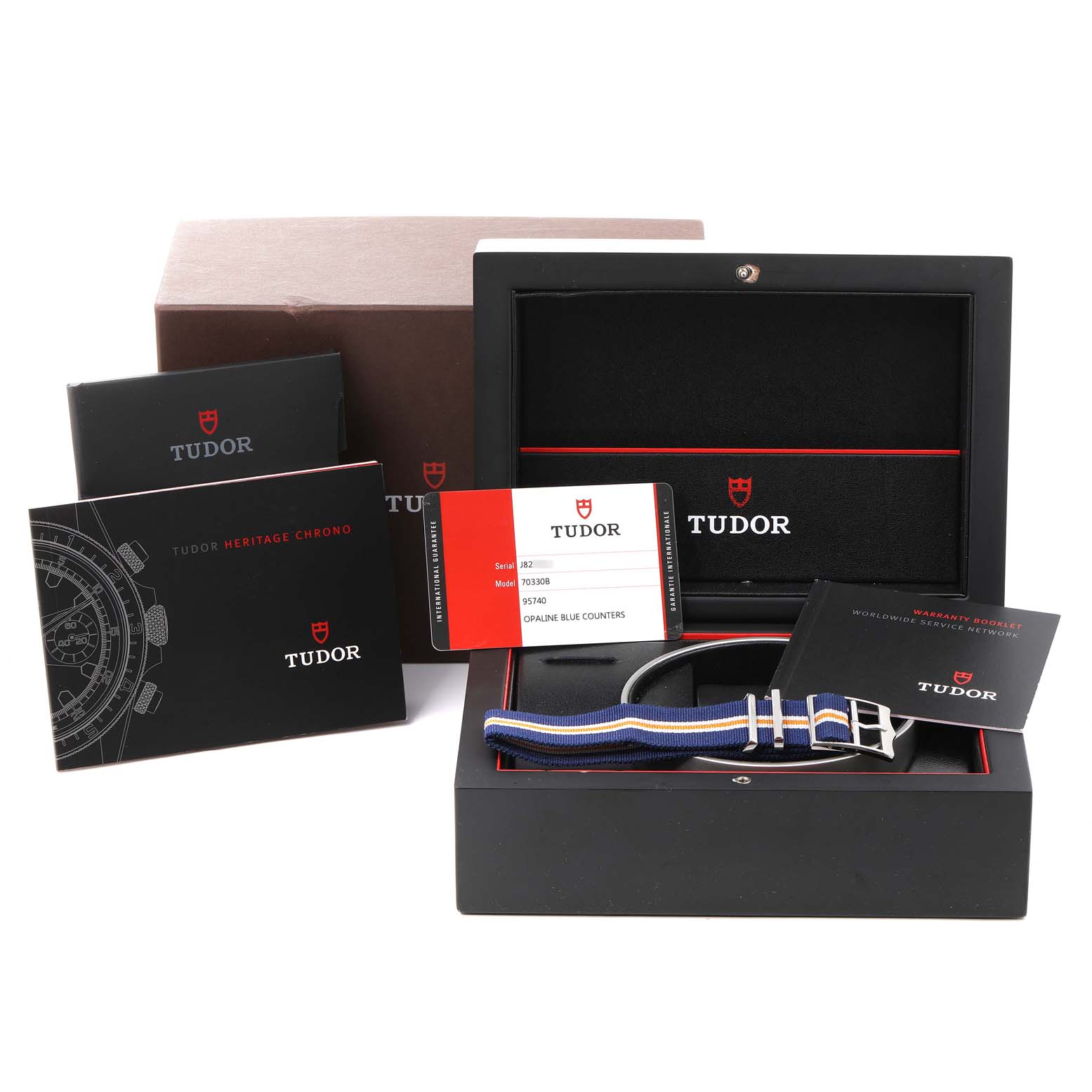 The image shows a Tudor Heritage Chrono 70330B Men's Stainless Steel Blue Dial 70330B Men's Stainless Steel Blue Dial watch set with its box, straps, warranty card, and booklets on display.