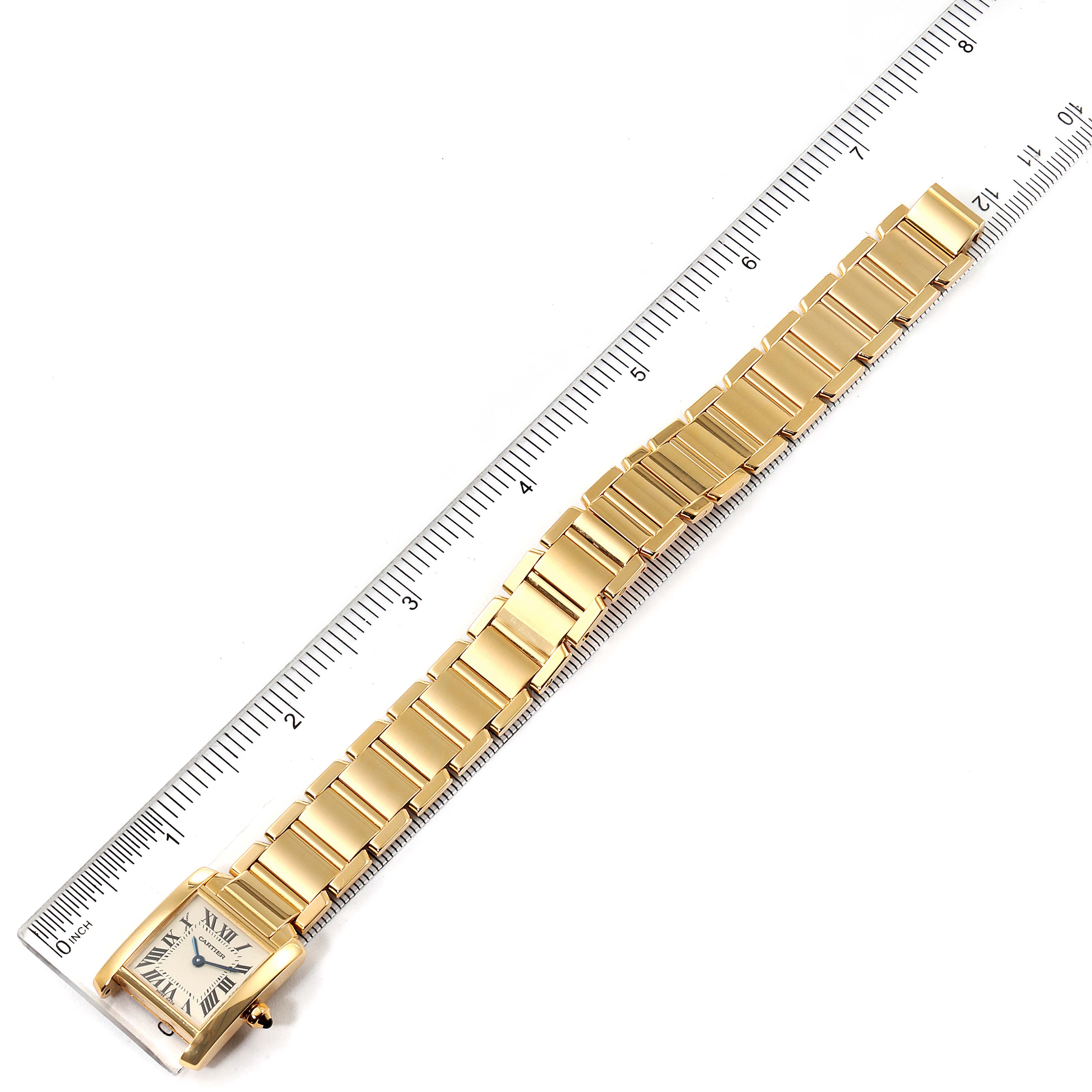 The image shows a Cartier Tank Française watch laid flat along a ruler, highlighting the entire gold bracelet and rectangular case.