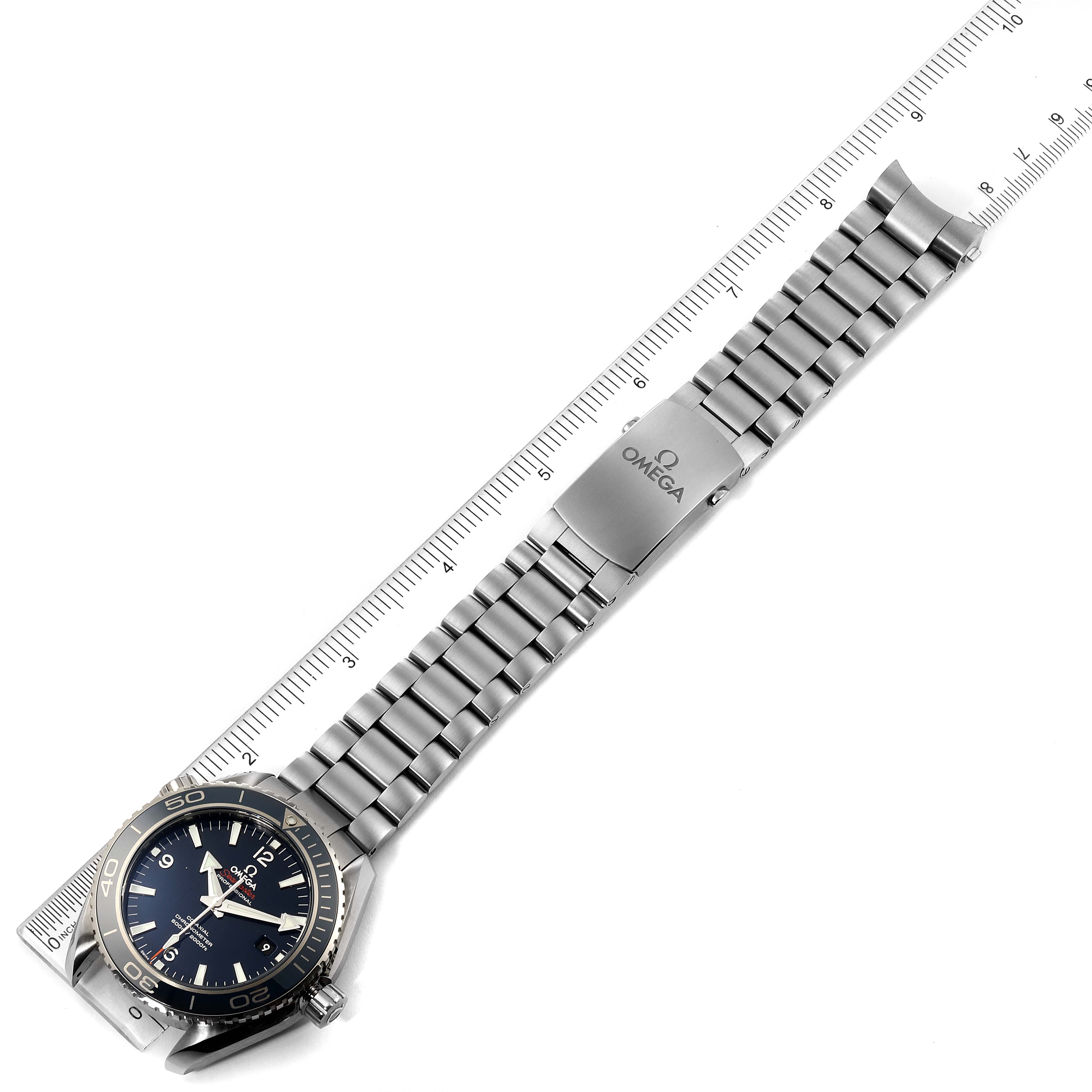 The image shows an overhead view of an Omega Planet Ocean 232.90.46.21.03.001 Men's Titanium Blue Dial 232.90.46.21.03.001 Men's Titanium Blue Dial watch with its metal bracelet and clasp visible next to a ruler.