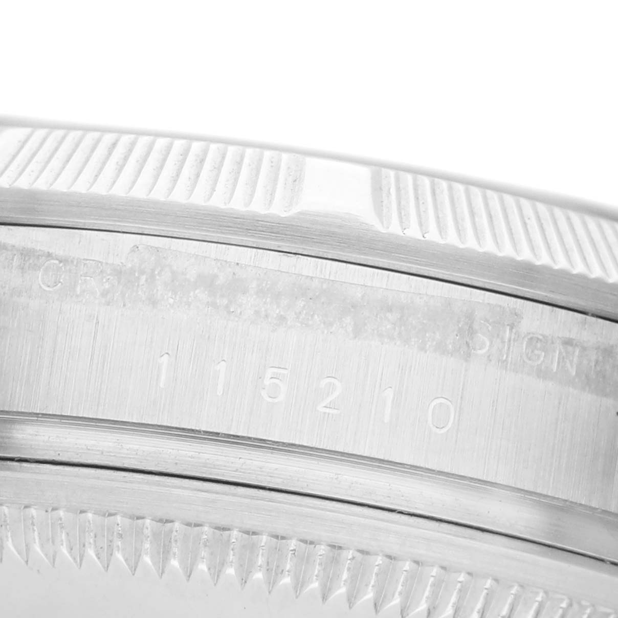 The image shows a close-up of the side of a Rolex Date 115210 Men's Stainless Steel Silver Dial watch, highlighting the engraved model number on the case.