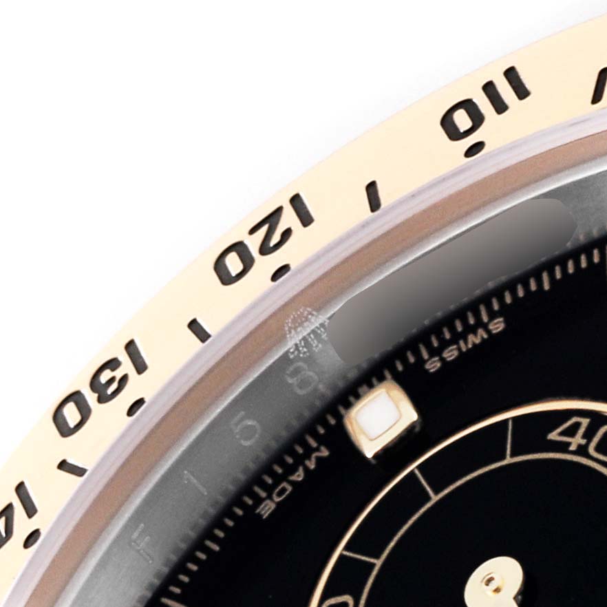 The image shows a close-up of the bezel and part of the dial of a Rolex Daytona 116523 Men's Steel and Gold (two tone) Black Dial 116523 Men's Steel and Gold (two tone) Black Dial watch.