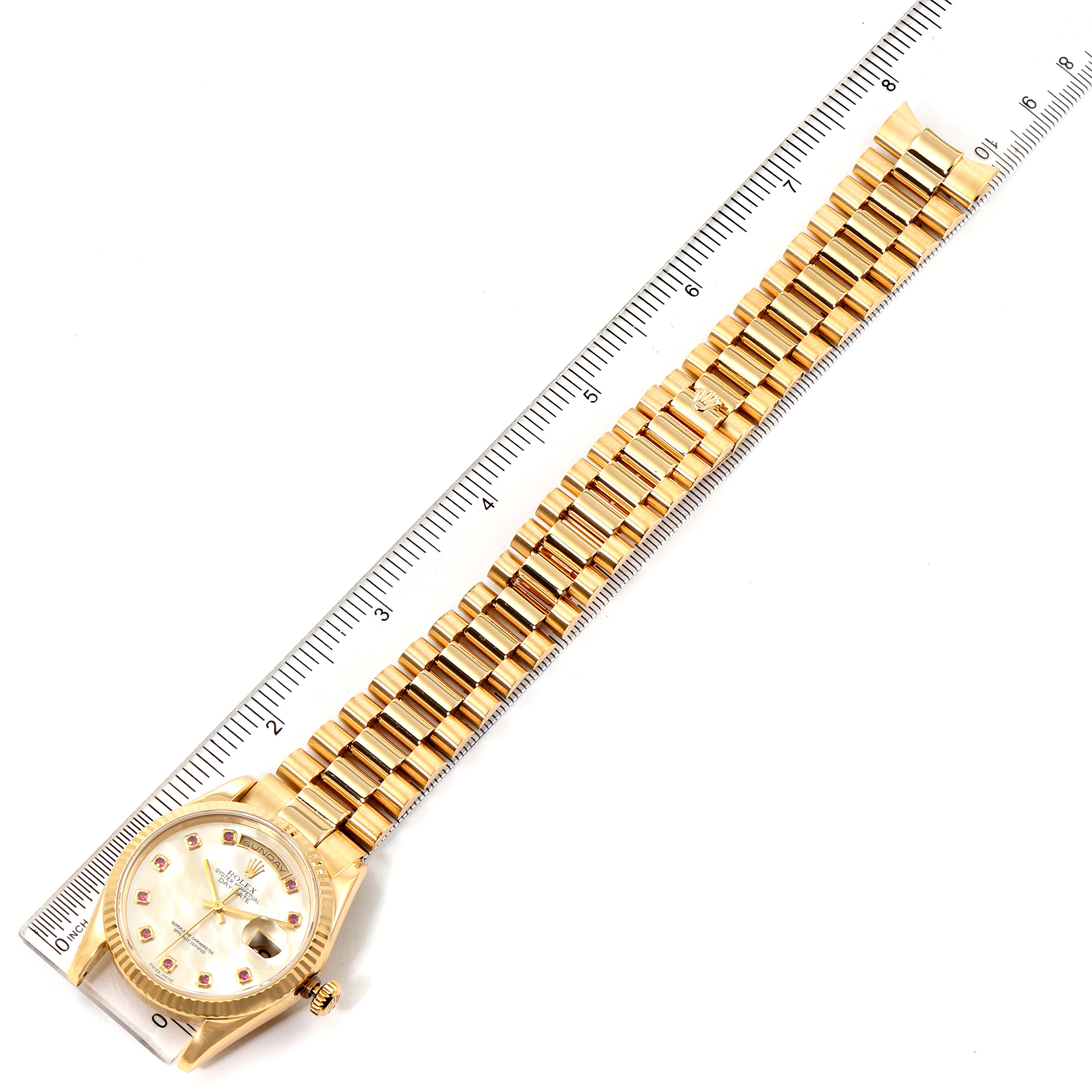 The image shows a Rolex President 118238 Men's Yellow Gold Mother of Pearl Dial 118238 Men's Yellow Gold Mother of Pearl Dial model watch viewed from the top, including its face and fully extended band next to a ruler.