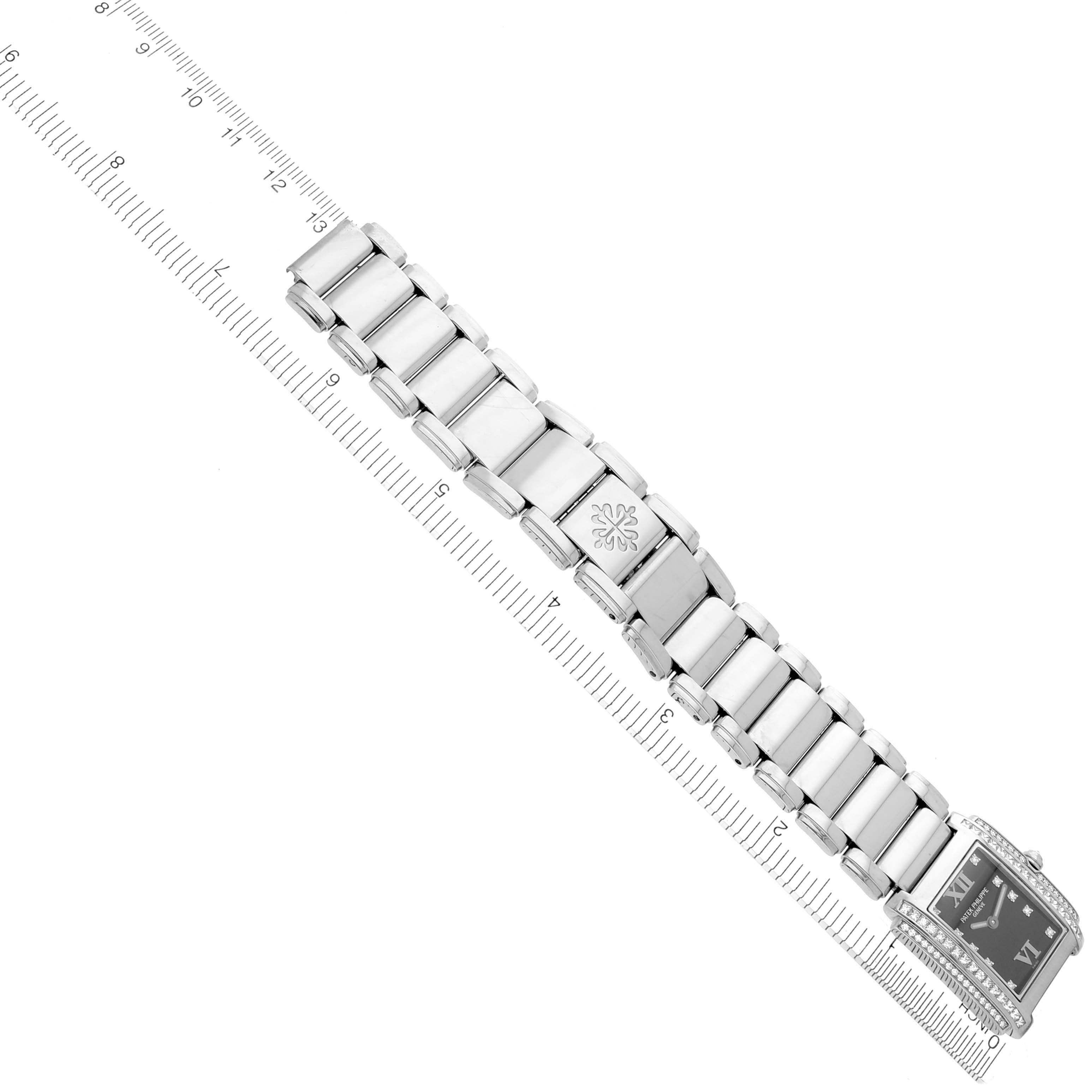 The image shows a top-down view of the Patek Philippe Twenty-4 4910/20G-011 Women's White Gold Black Dial 4910/20G-011 Women's White Gold Black Dial watch, highlighting the bracelet and face next to a ruler.