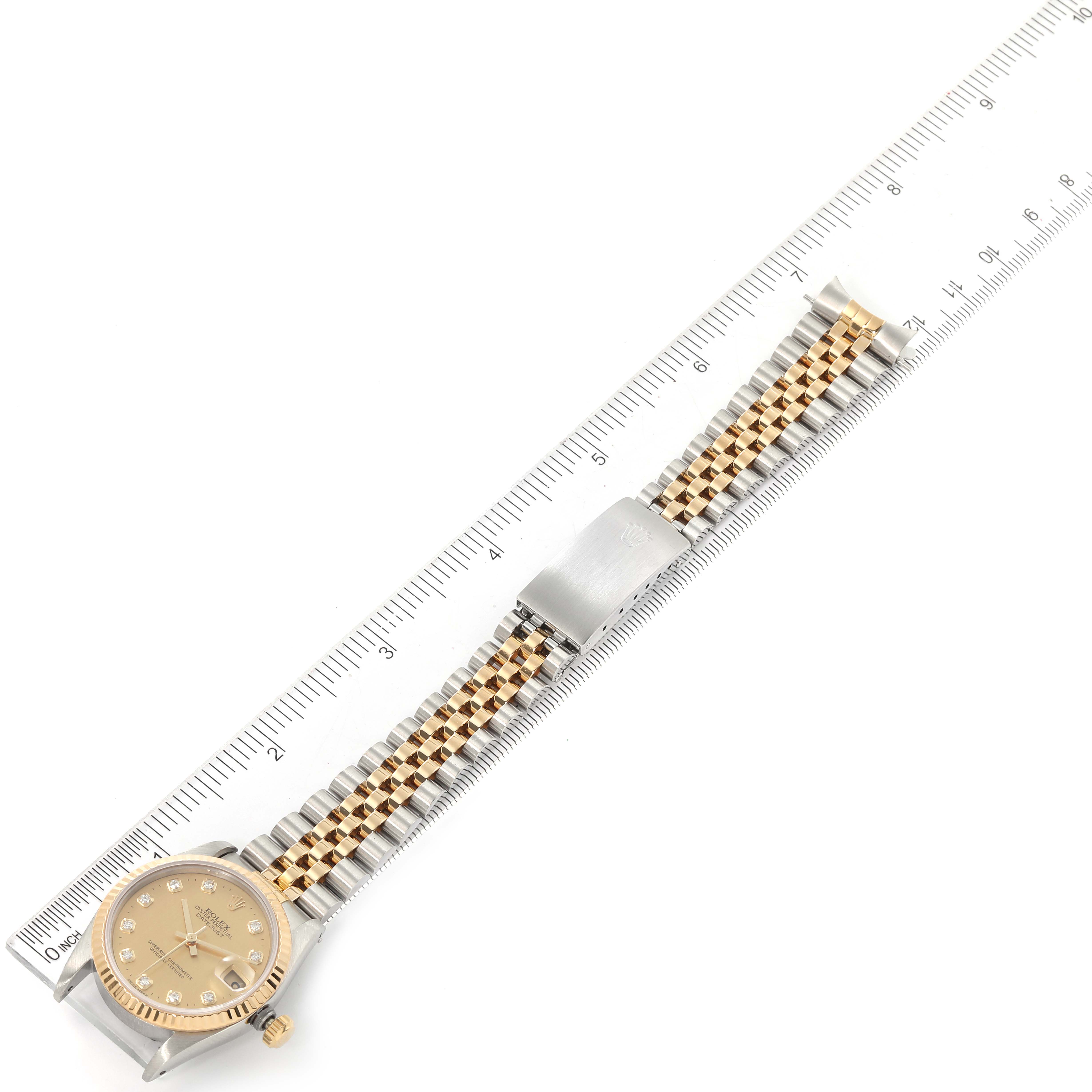 The image shows a Rolex Mid-Size 68273 Women
s Steel and Gold (two tone) Champagne Dial 68273 Women
s Steel and Gold (two tone) Champagne Dial watch placed next to a ruler, highlighting the face, bracelet, and clasp from a top-down angle.