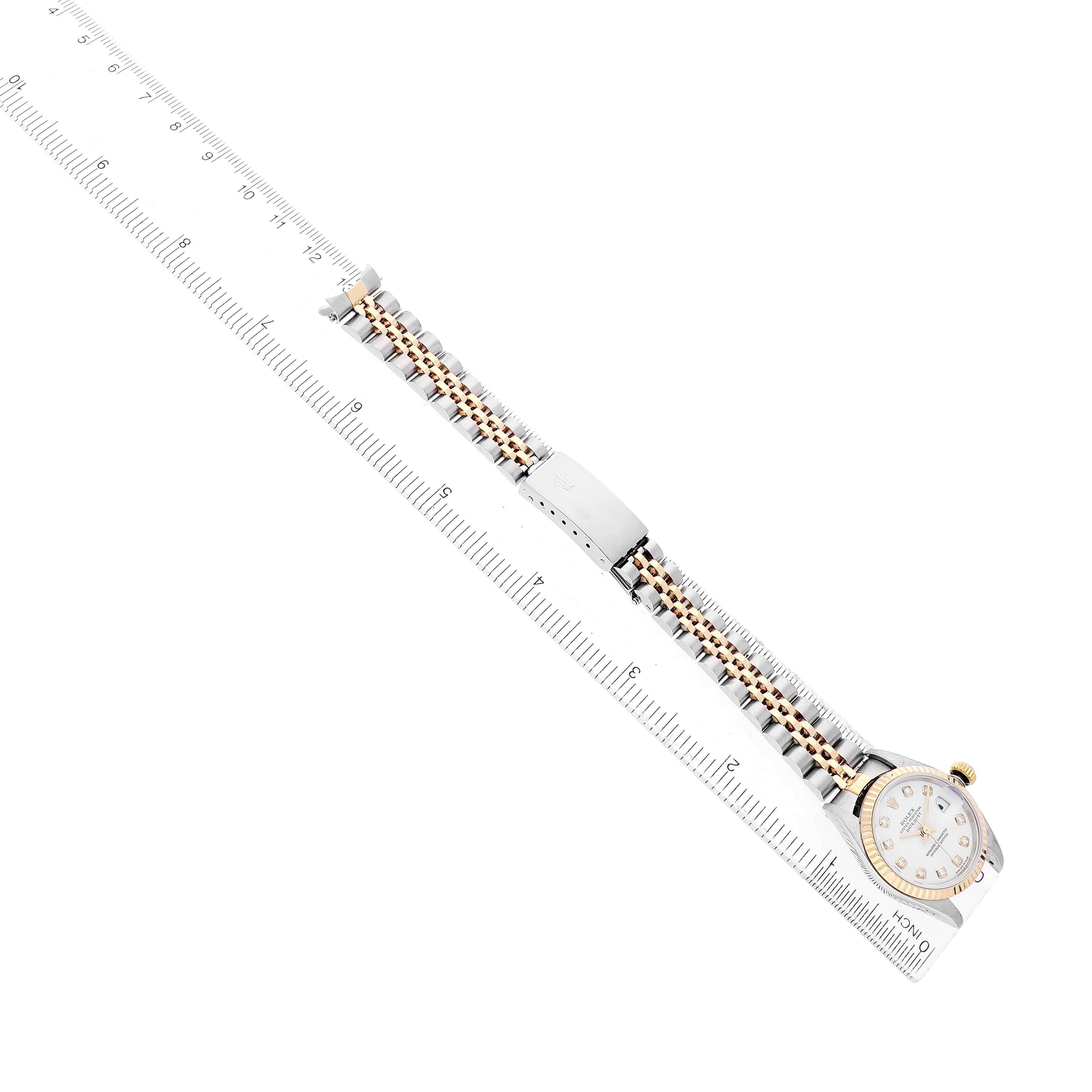 The Rolex Datejust 79173 Women's Steel and Gold (two tone) White Dial watch is shown from a top-down angle, highlighting the face, bracelet, and clasp on a ruler for scale.