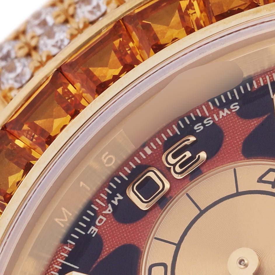 The image shows a close-up of the dial and part of the crystal-bezel on a Rolex Daytona 116598 Men's Yellow Gold Orange Dial, highlighting orange gemstones and the 30-minute marker.