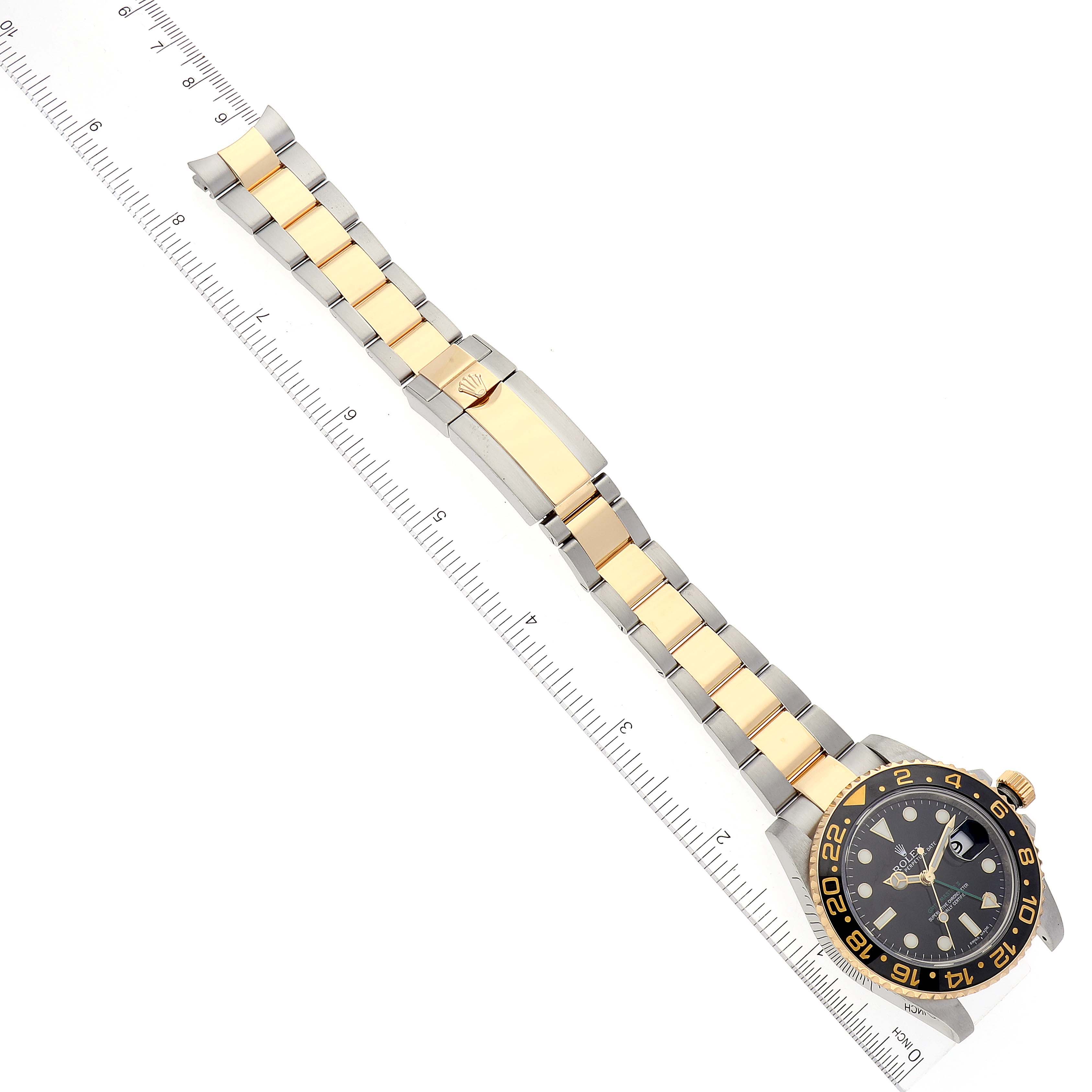 The image shows a Rolex GMT-Master 116713 Men's Steel and Gold (two tone) Black Dial 116713 Men's Steel and Gold (two tone) Black Dial watch laid flat alongside a ruler, showcasing its full bracelet and face at an angled view.