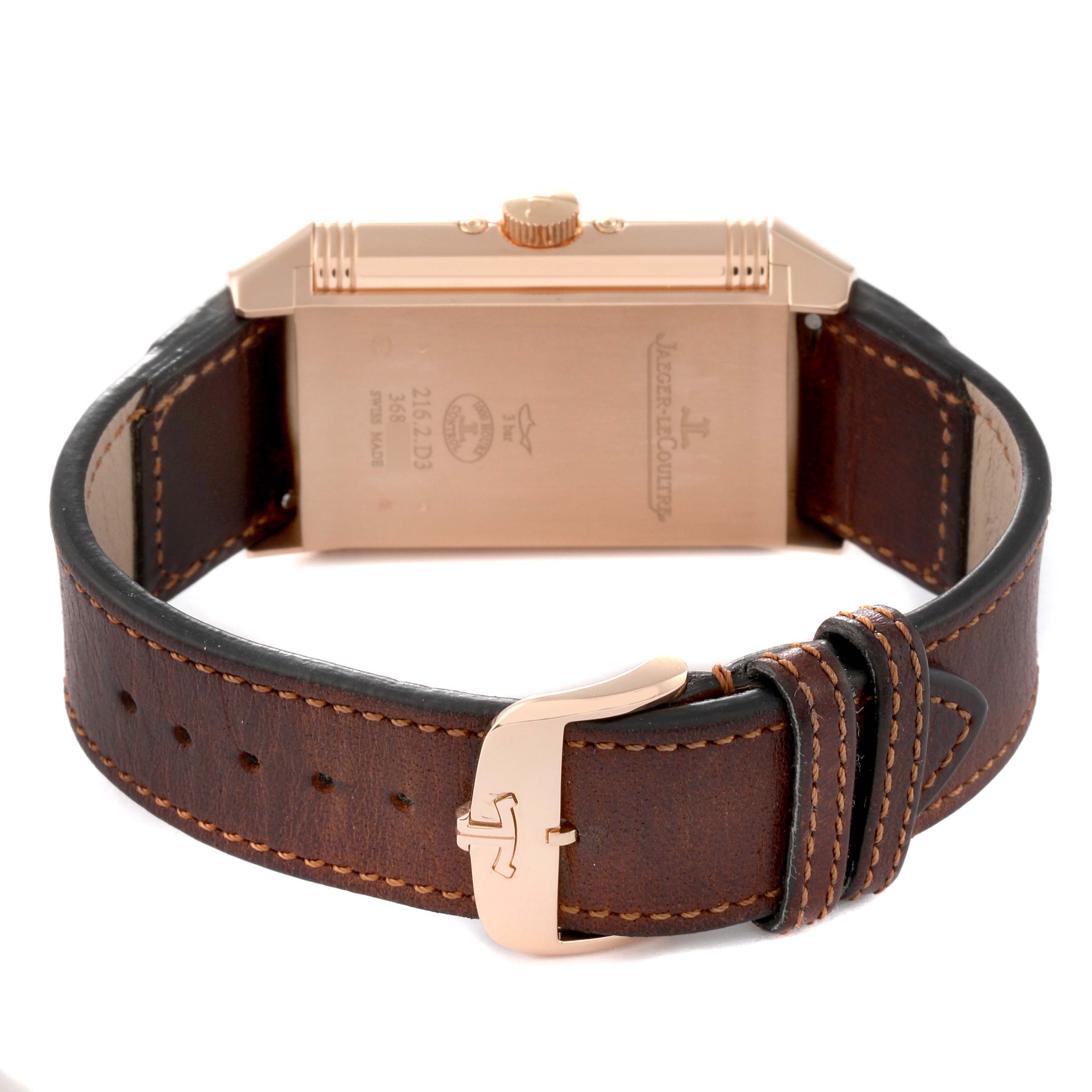 The image shows the back view of a Jaeger LeCoultre Reverso Q3912530 Men's Rose Gold Silver Dial Q3912530 Men's Rose Gold Silver Dial watch, highlighting the watch case, crown, and leather strap with stitching and a buckle.