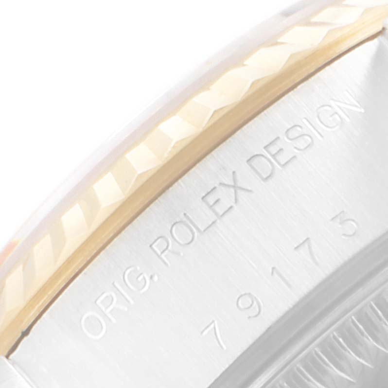 This close-up image shows the side of a Rolex Datejust 79173 Women
s Steel and Gold (two tone) Champagne Dial 79173 Women
s Steel and Gold (two tone) Champagne Dial watch, highlighting the engraved text and part of the fluted bezel.