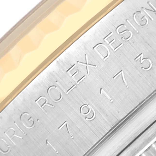 The image shows a close-up of the side of a Rolex Datejust 179173 Women
s Steel and Gold (two tone) White Dial 179173 Women
s Steel and Gold (two tone) White Dial watch case with engraved text and part of the fluted bezel.
