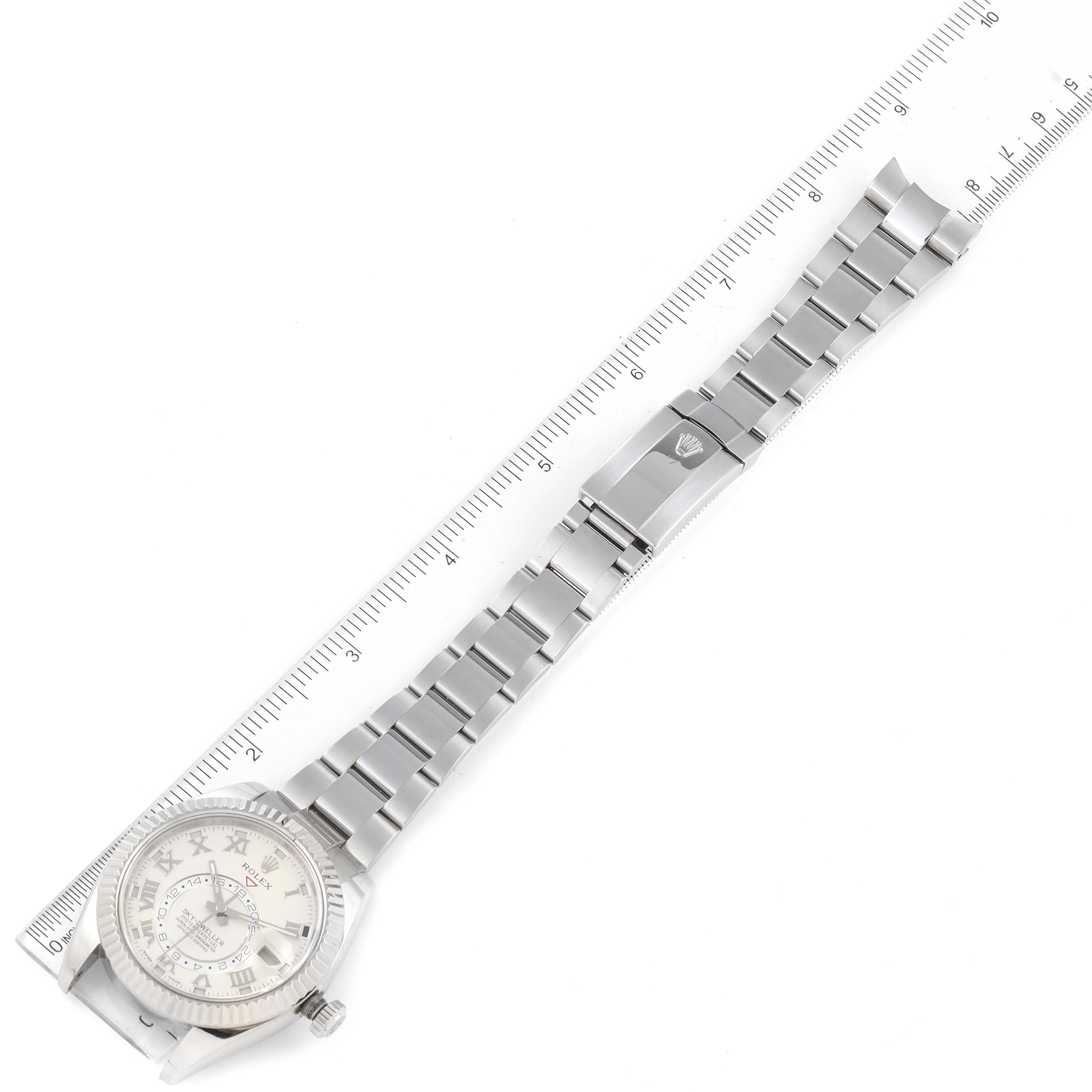 The image shows an overhead view of a Rolex Sky-Dweller 326939 Men's White Gold White Dial 326939 Men's White Gold White Dial watch with its face and full metal bracelet alongside a ruler.