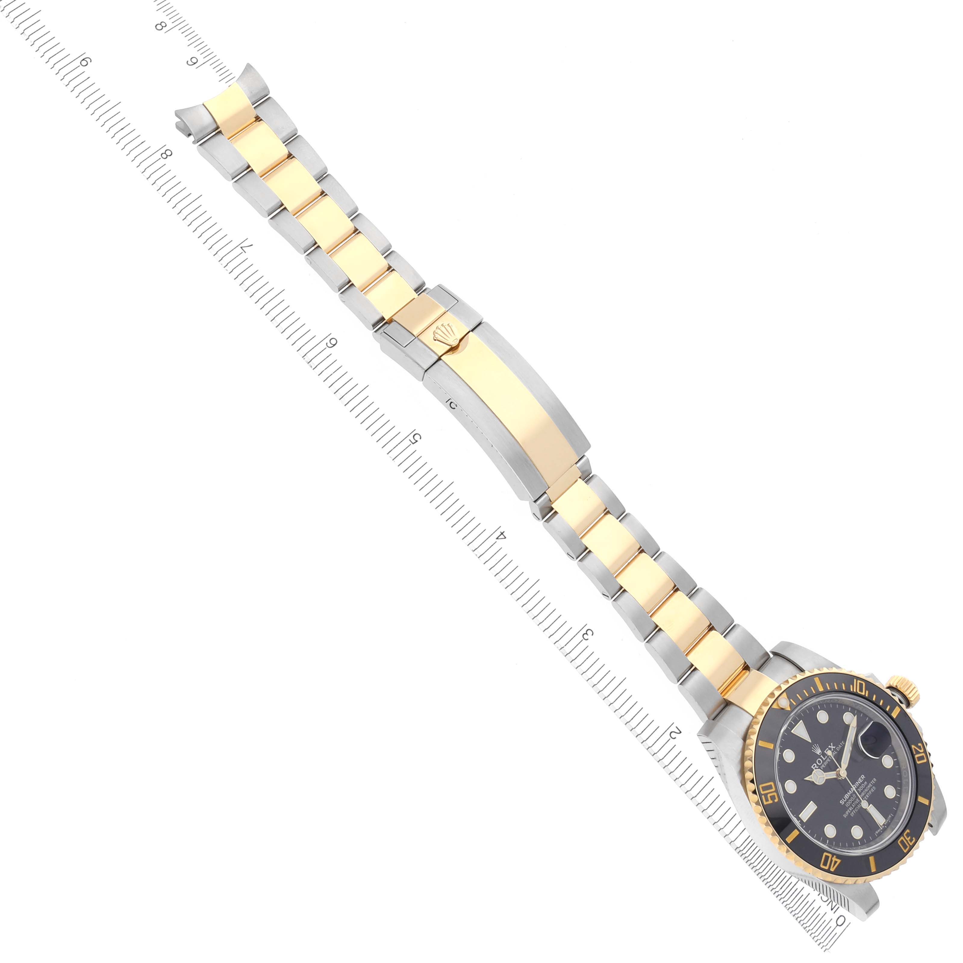 The Rolex Submariner 116613LN Men's Steel and Gold (two tone) Black Dial 116613LN Men's Steel and Gold (two tone) Black Dial watch is shown from an overhead angle, displaying the bracelet and face next to a ruler for scale.