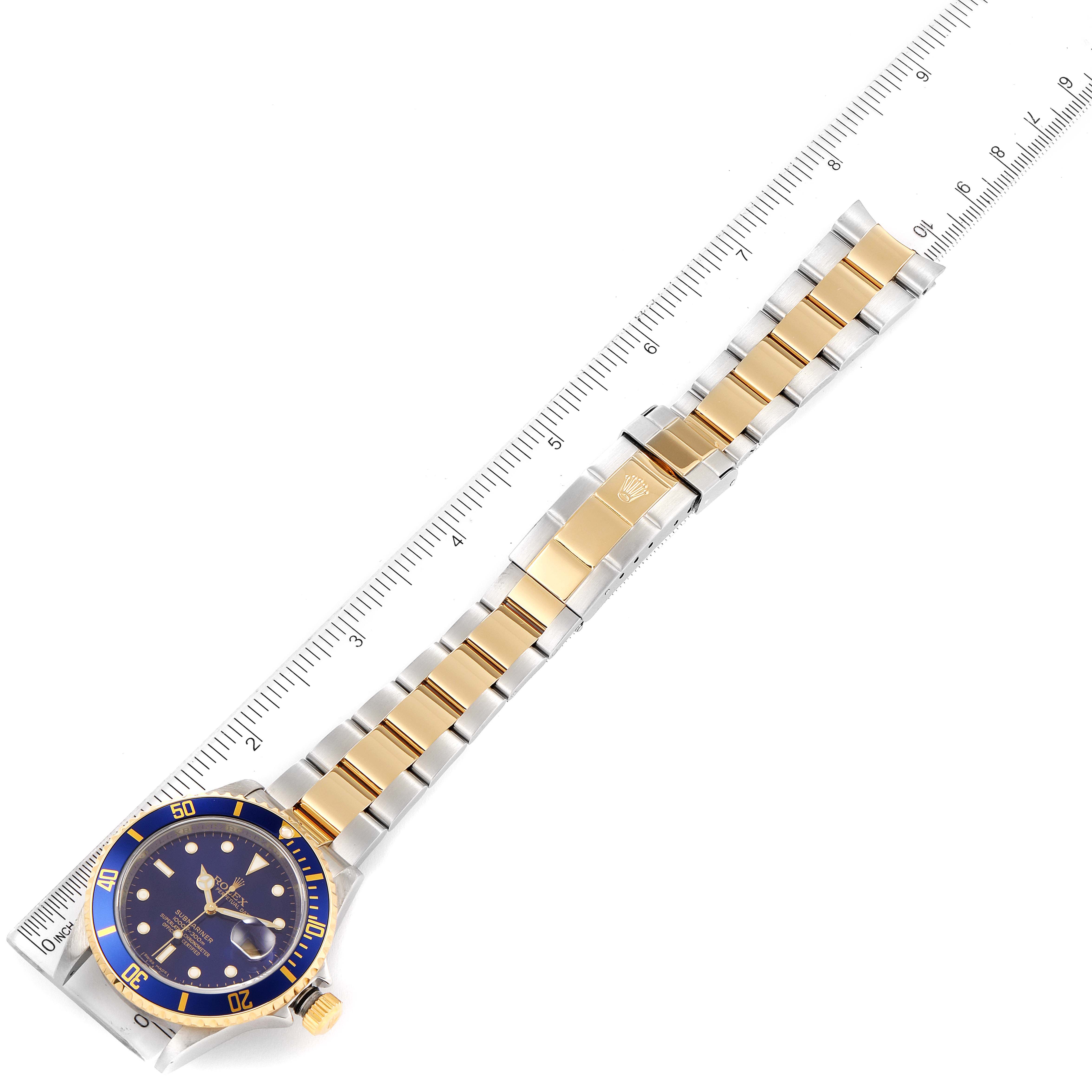 The image shows a top-down view of a Rolex Submariner 16613 Men's Steel and Gold (two tone) Blue Dial 16613 Men's Steel and Gold (two tone) Blue Dial watch with a two-tone bracelet beside a ruler.