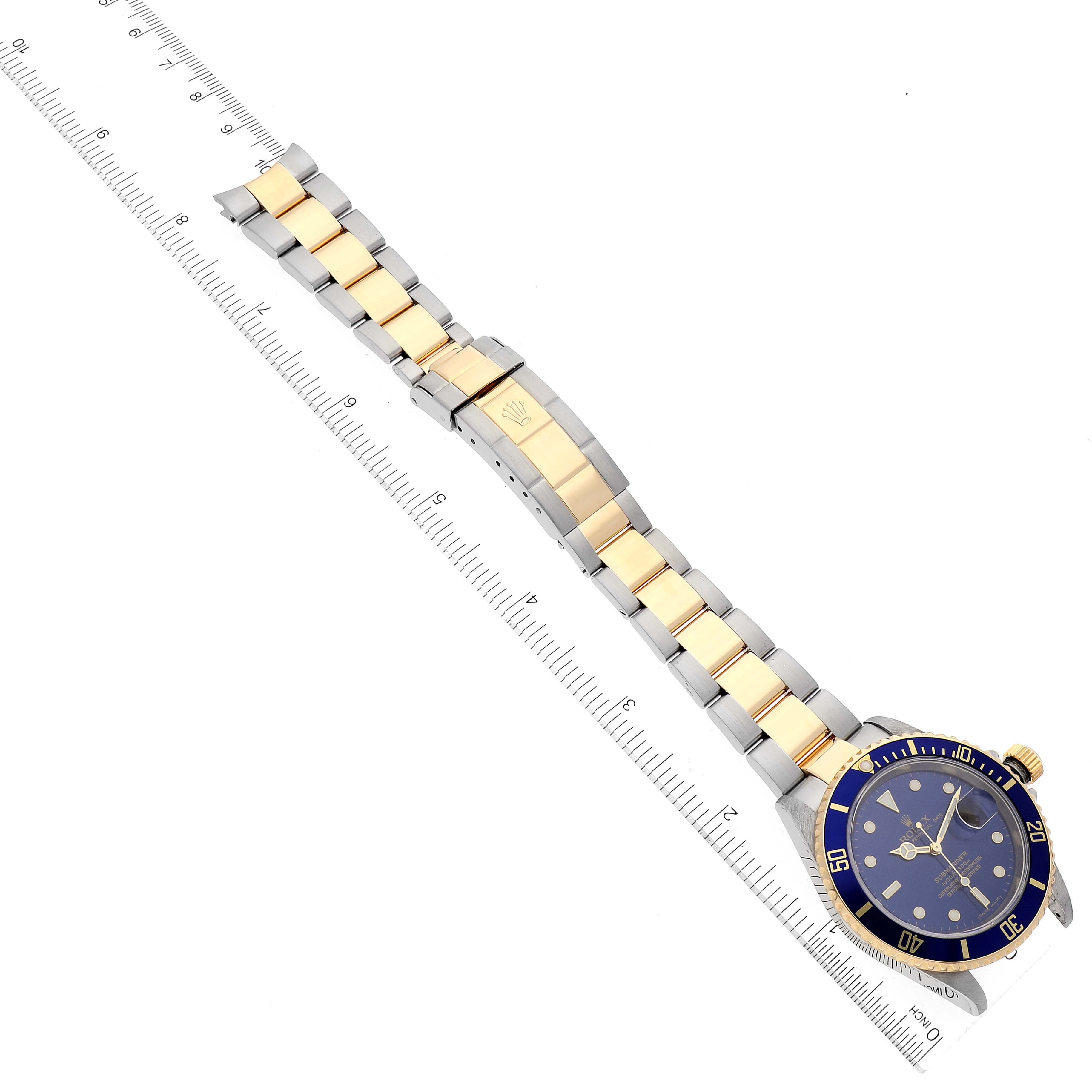 The image shows a Rolex Submariner 16613 Men's Steel and Gold (two tone) Blue Dial 16613 Men's Steel and Gold (two tone) Blue Dial watch laid flat, showcasing the bracelet, clasp, and dial, next to a ruler for scale.