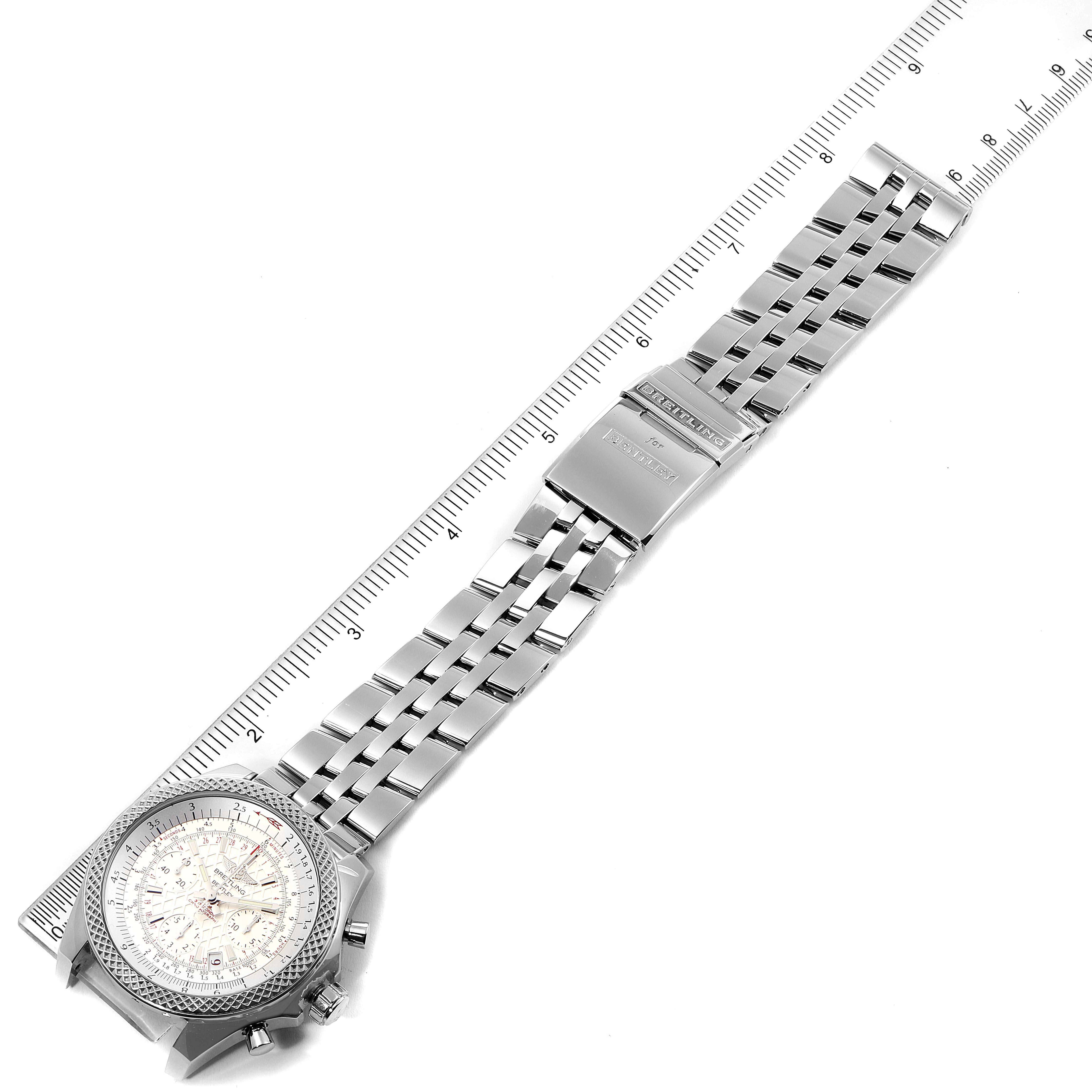 The Breitling Bentley AB061221/G810-980A Men's Stainless Steel Silver Dial AB061221/G810-980A Men's Stainless Steel Silver Dial watch is shown from an angled top-down view, displaying the face, metal bracelet, and clasp alongside a ruler.