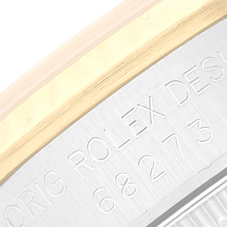This image shows a close-up of the side casing of a Rolex Mid-Size 68273 Women
s Steel and Gold (two tone) Champagne Dial 68273 Women
s Steel and Gold (two tone) Champagne Dial watch, displaying engraved text and part of the bezel.