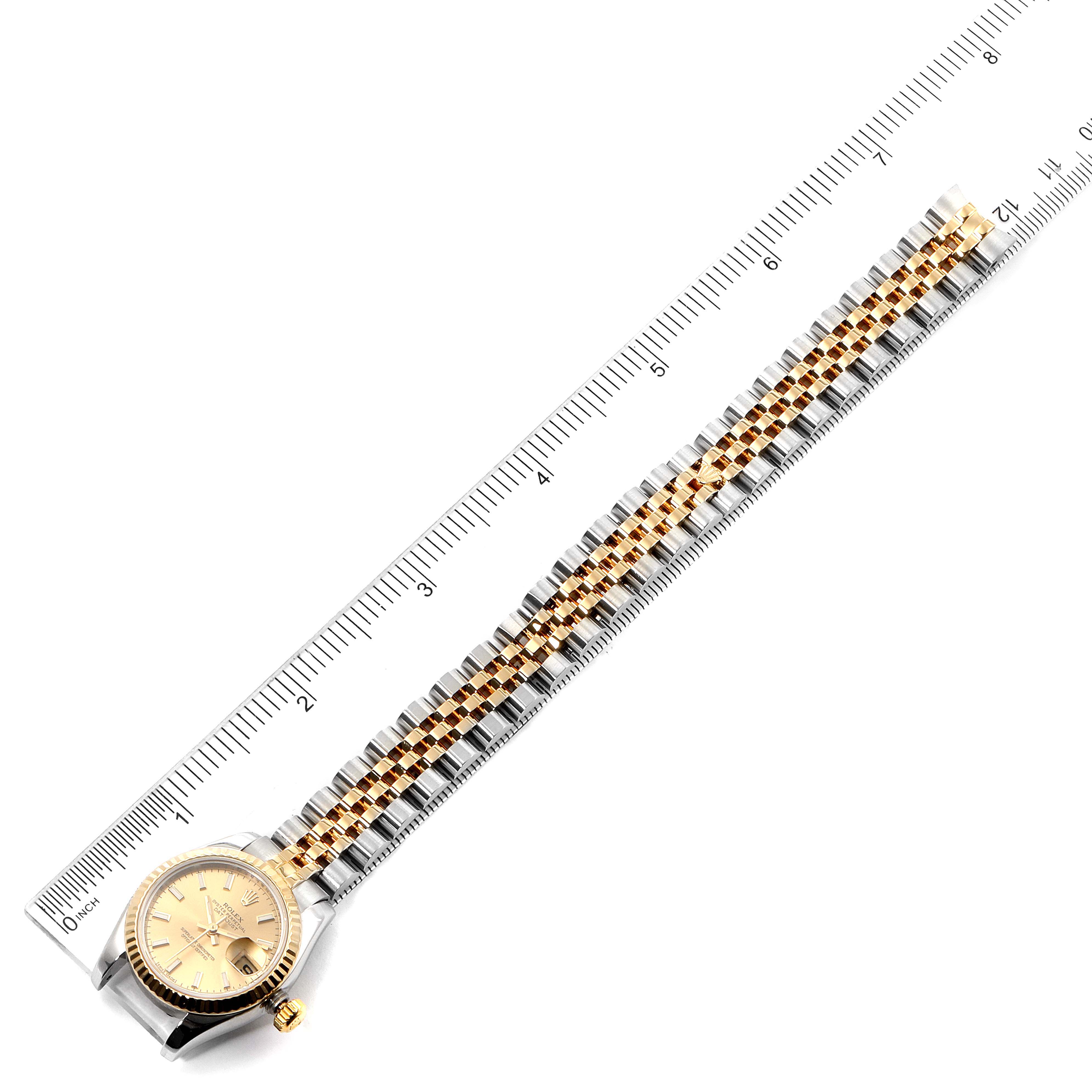 The Rolex Datejust 179173 Women
s Steel and Gold (two tone) Champagne Dial 179173 Women
s Steel and Gold (two tone) Champagne Dial watch is shown from a top-down angle, displaying its face, bezel, and full linked bracelet, with a ruler alongside for scale.