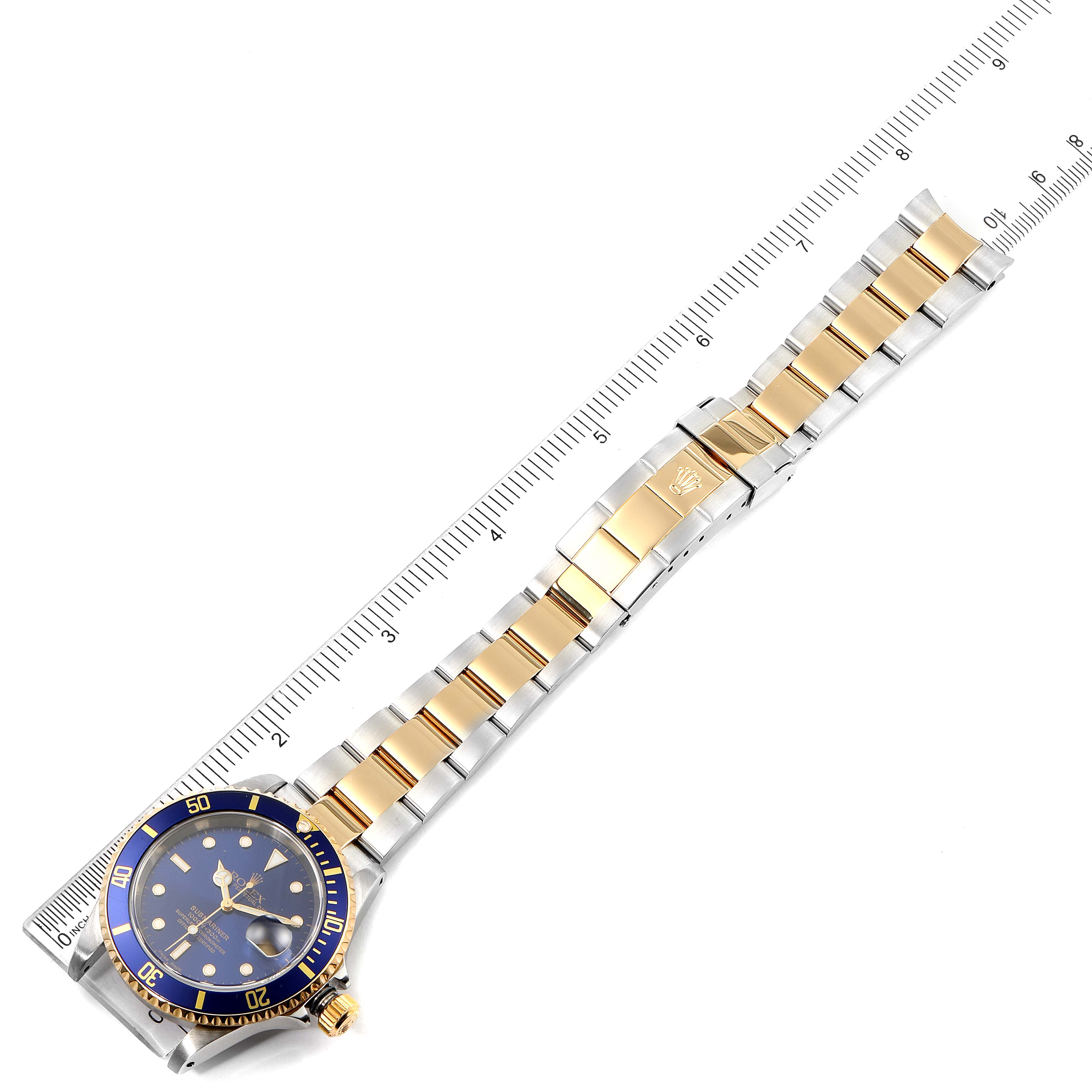 The image shows a top-down view of a Rolex Submariner 16613 Men's Steel and Gold (two tone) Blue Dial 16613 Men's Steel and Gold (two tone) Blue Dial watch with a two-tone bracelet, alongside a measuring ruler.