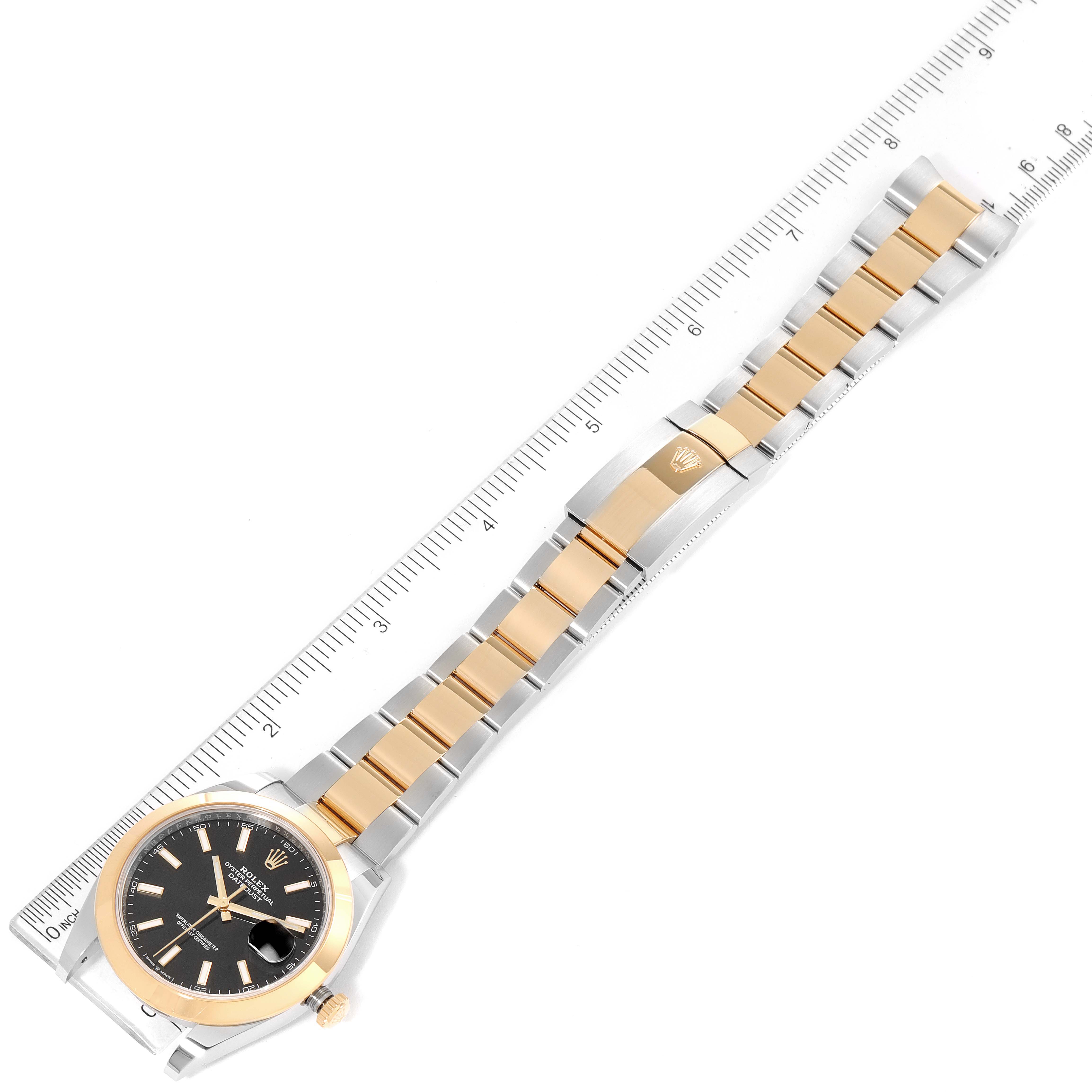 The image shows the full length of a Rolex Datejust 41 126303 Men's Steel and Gold (two tone) Black Dial 126303 Men's Steel and Gold (two tone) Black Dial watch from the top, with emphasis on the band and face laid next to a ruler.