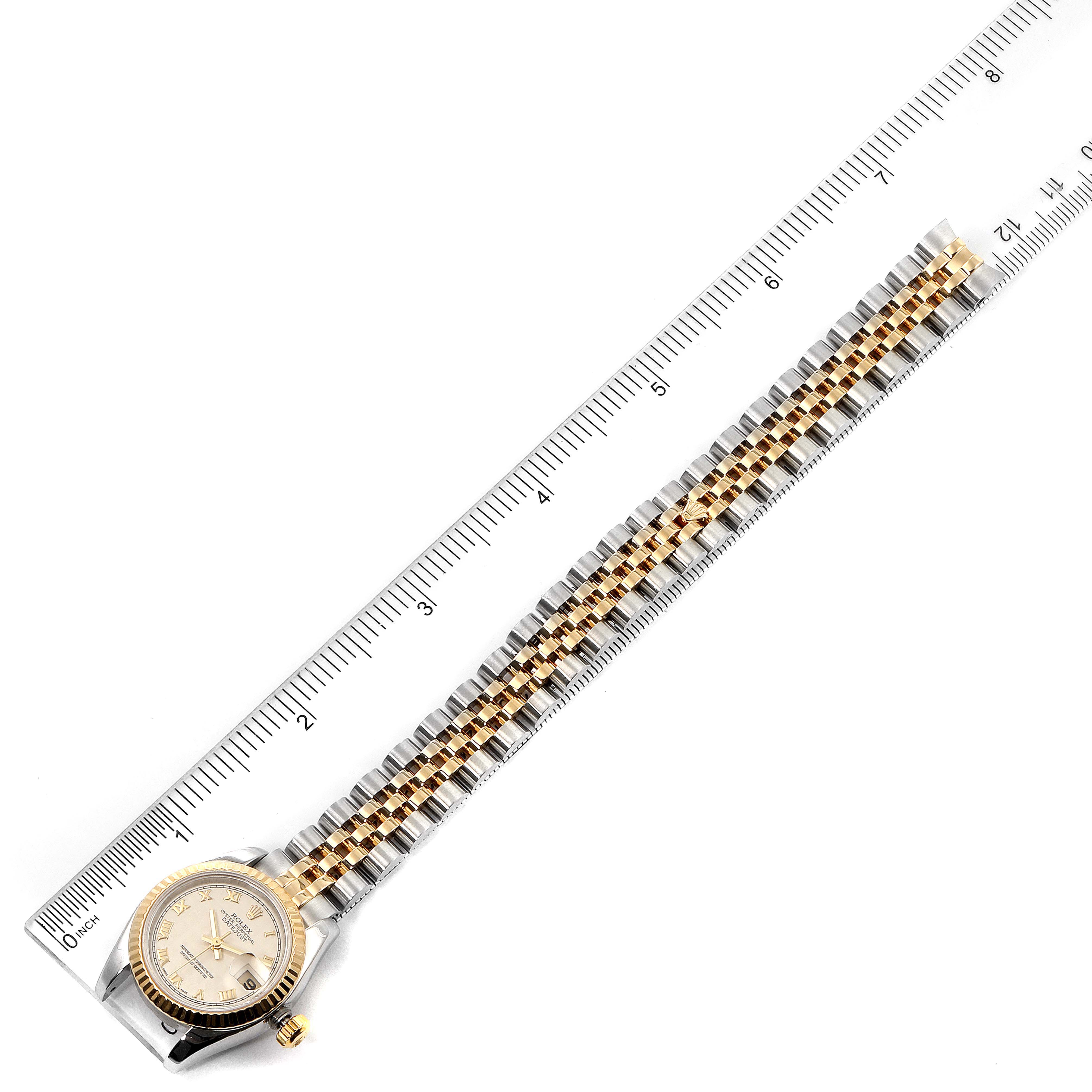 The image shows the front view of a Rolex Datejust 179173 Women
s Steel and Gold (two tone) Silver Dial 179173 Women
s Steel and Gold (two tone) Silver Dial watch, including the face and bi-metal bracelet, positioned next to a ruler.