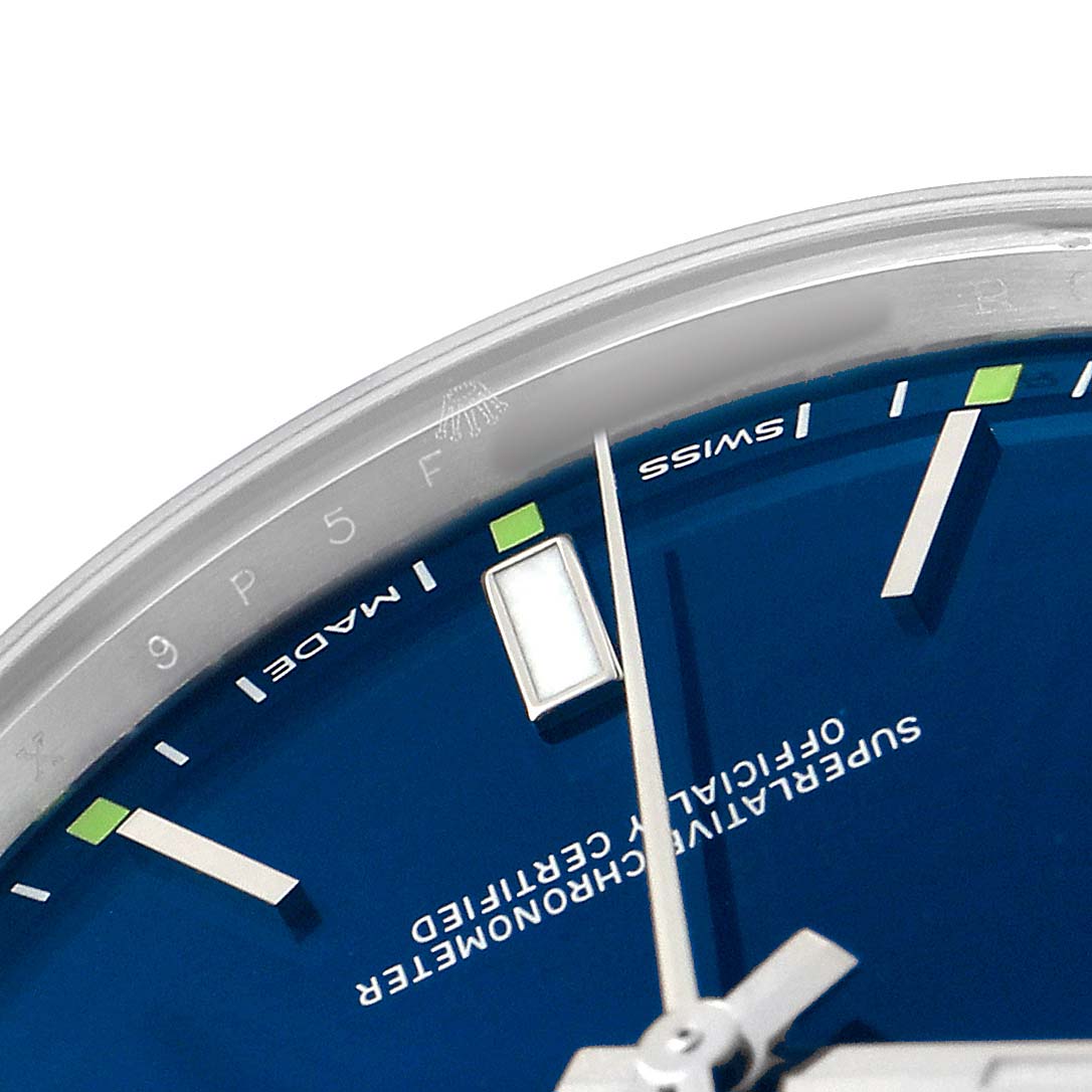 The image shows a close-up of the upper right section of a Rolex Oyster Perpetual 114300 Men's Stainless Steel Blue Dial watch, focusing on the dial and hour markers.