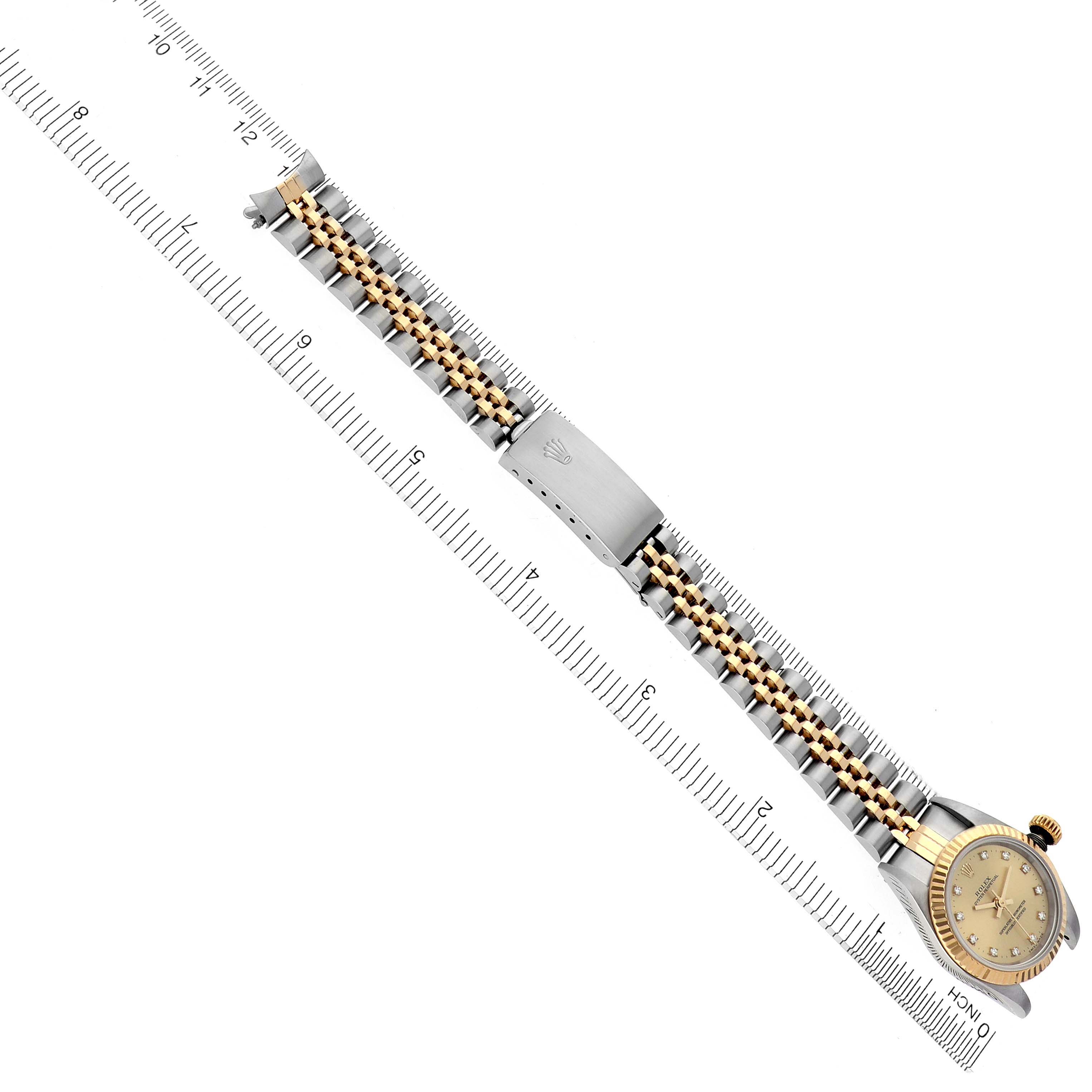 The Rolex Oyster Perpetual 67193 Women's Steel and Gold (two tone) Champagne Dial 67193 Women's Steel and Gold (two tone) Champagne Dial watch is shown in a flat, diagonal angle displaying its face and entire bracelet next to a measuring ruler.