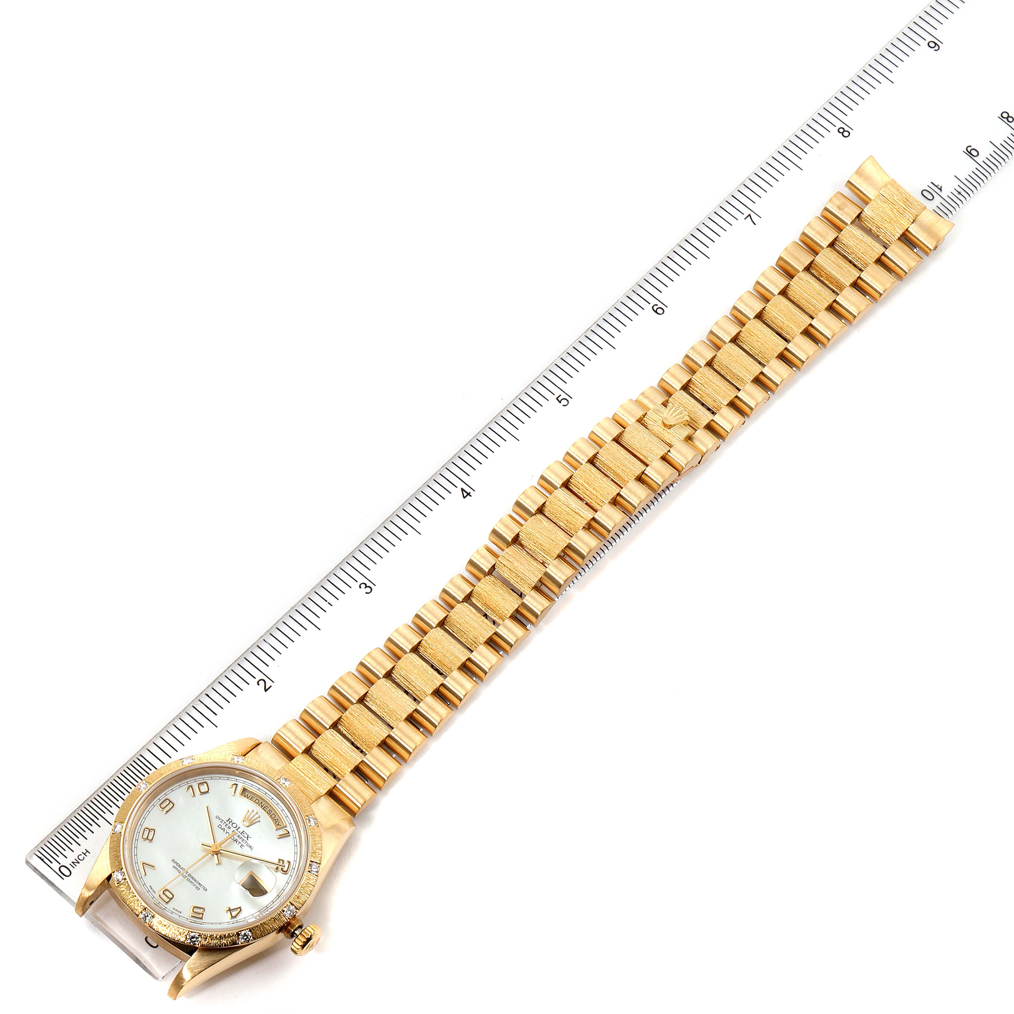 The image shows a top view of a Rolex President 18308 Men
s Yellow Gold Mother of Pearl Dial 18308 Men
s Yellow Gold Mother of Pearl Dial model watch with its band extended alongside a ruler.