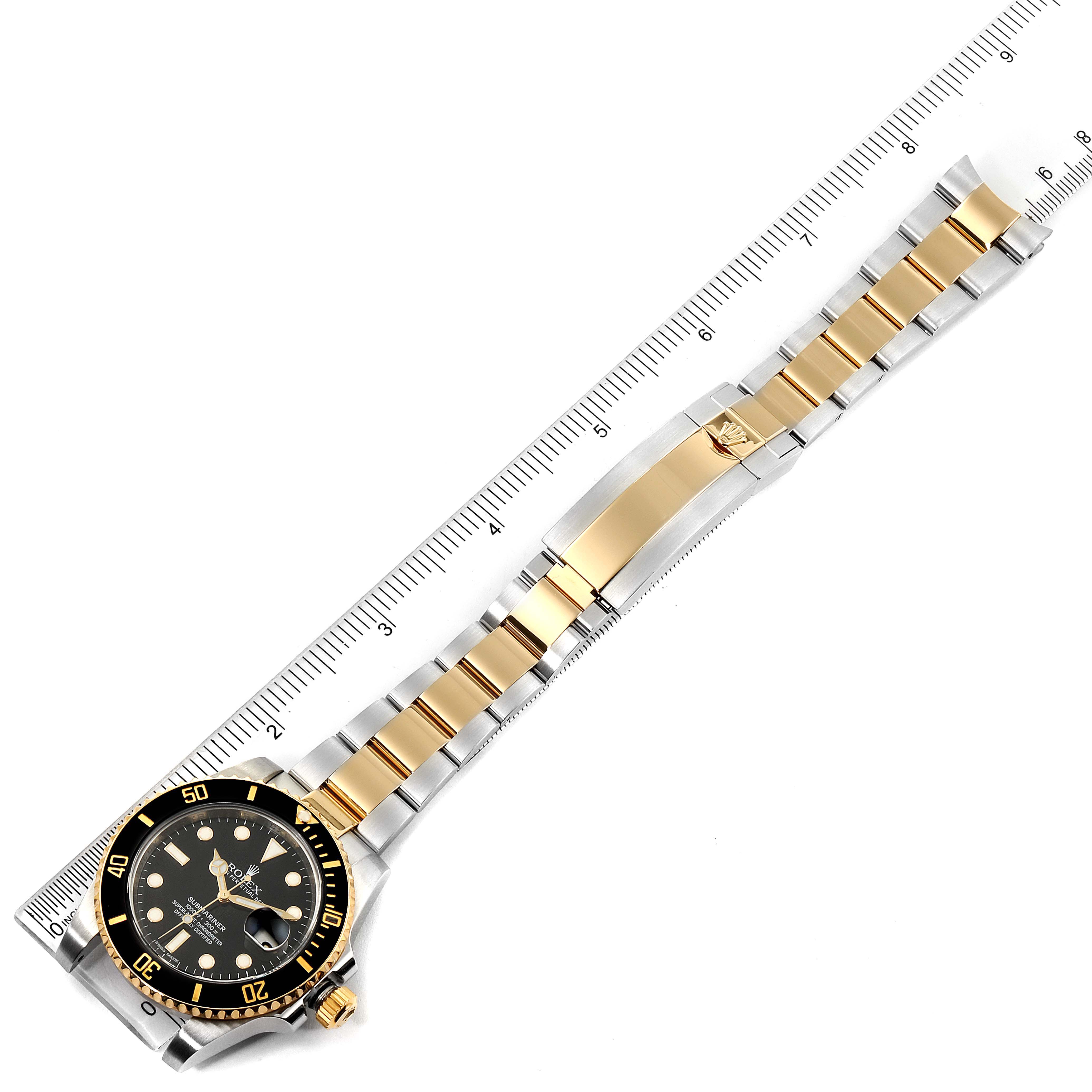 This image shows a Rolex Submariner 116613 Men's Steel and Gold (two tone) Black Dial 116613 Men's Steel and Gold (two tone) Black Dial watch laid flat with the strap extended alongside a ruler, displaying the bracelet and dial.