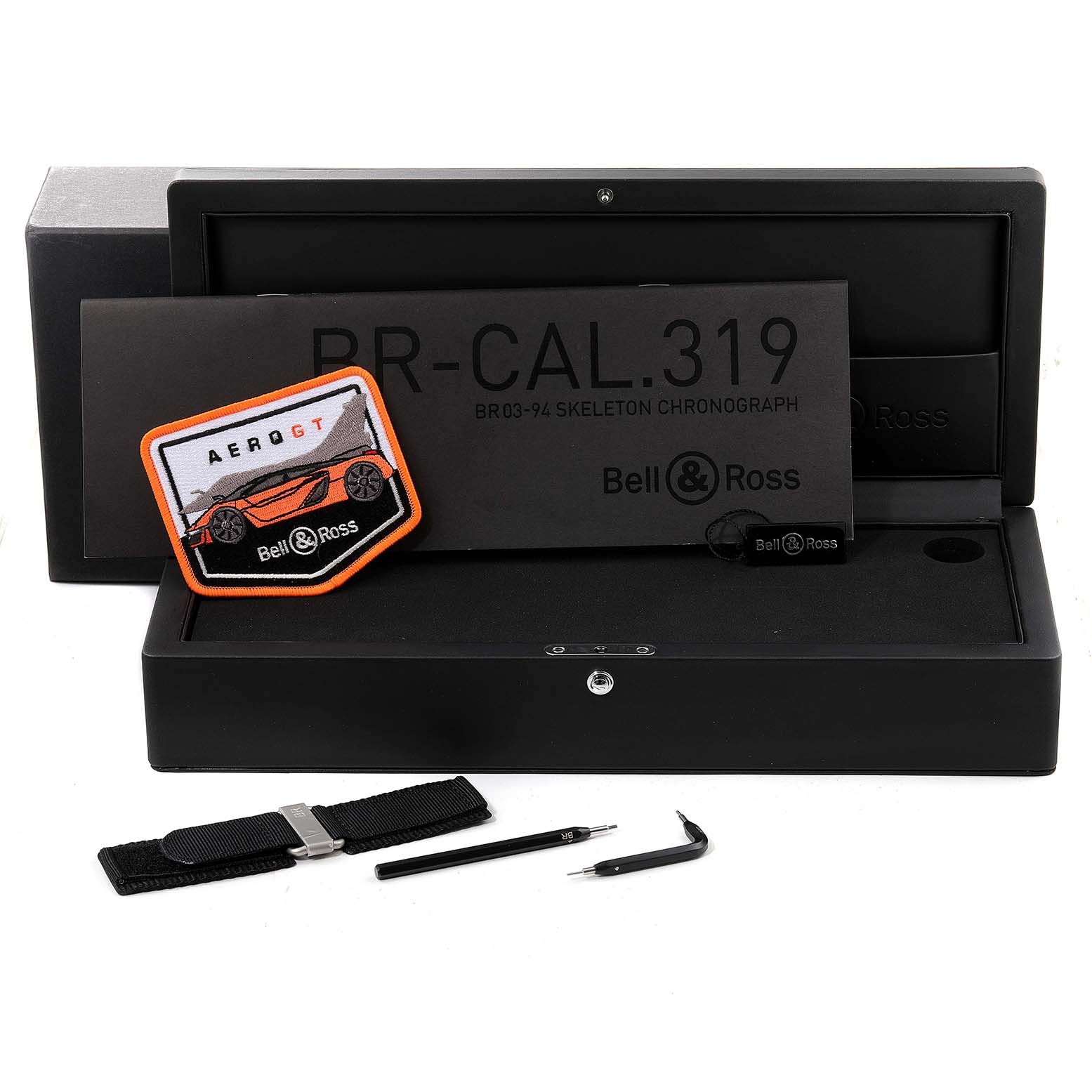 The image shows the packaging, strap, tools, and patch for the Bell & Ross Aero GT Orange Skeleton Steel Mens Watch BR0394 model.