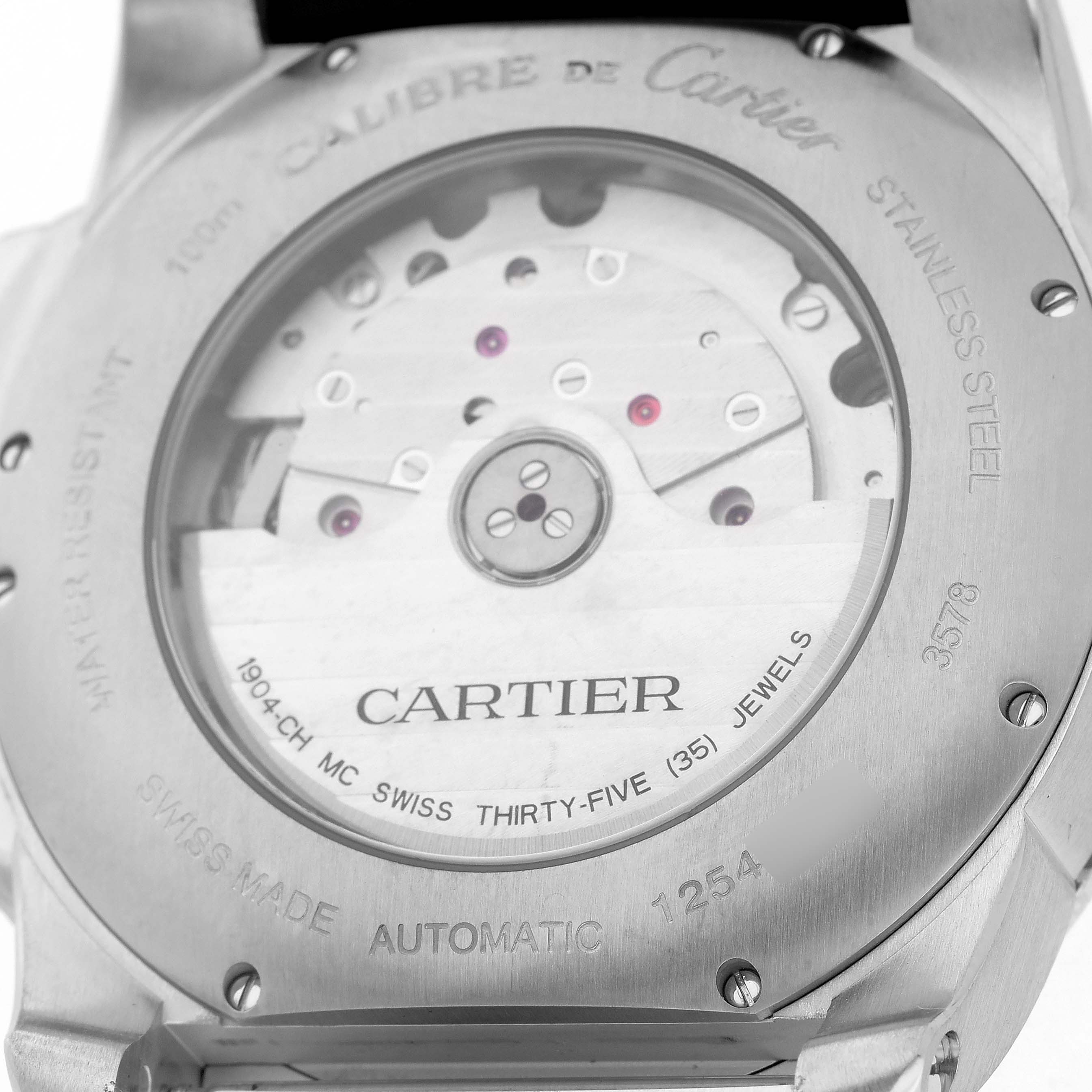 The image shows a back view of the Calibre de Cartier watch, highlighting the automatic movement and inscriptions.