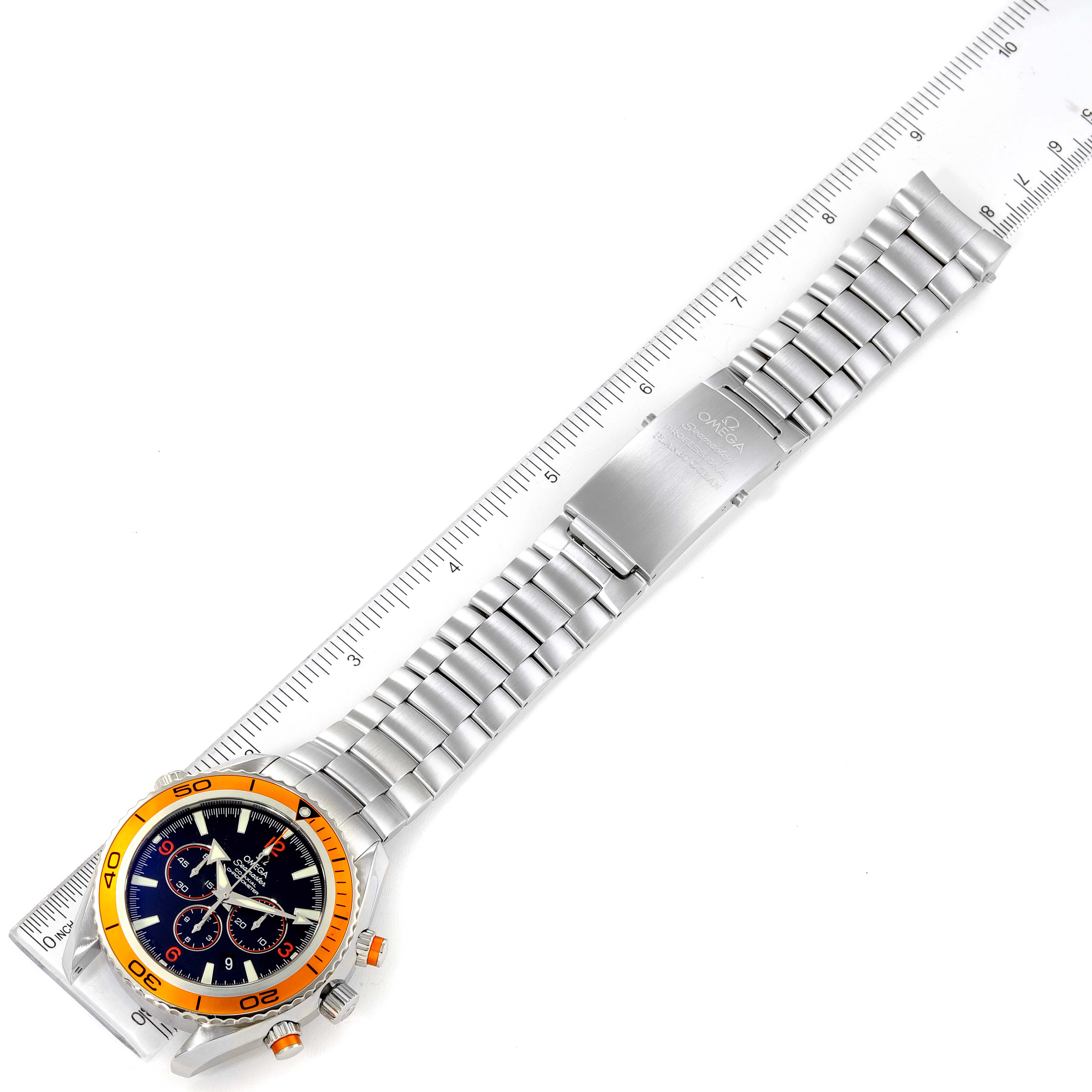 The image shows an Omega Planet Ocean 2218.50.00 Men
s Stainless Steel Black Dial 2218.50.00 Men
s Stainless Steel Black Dial watch laid flat with its stainless steel strap extended next to a ruler for scale.