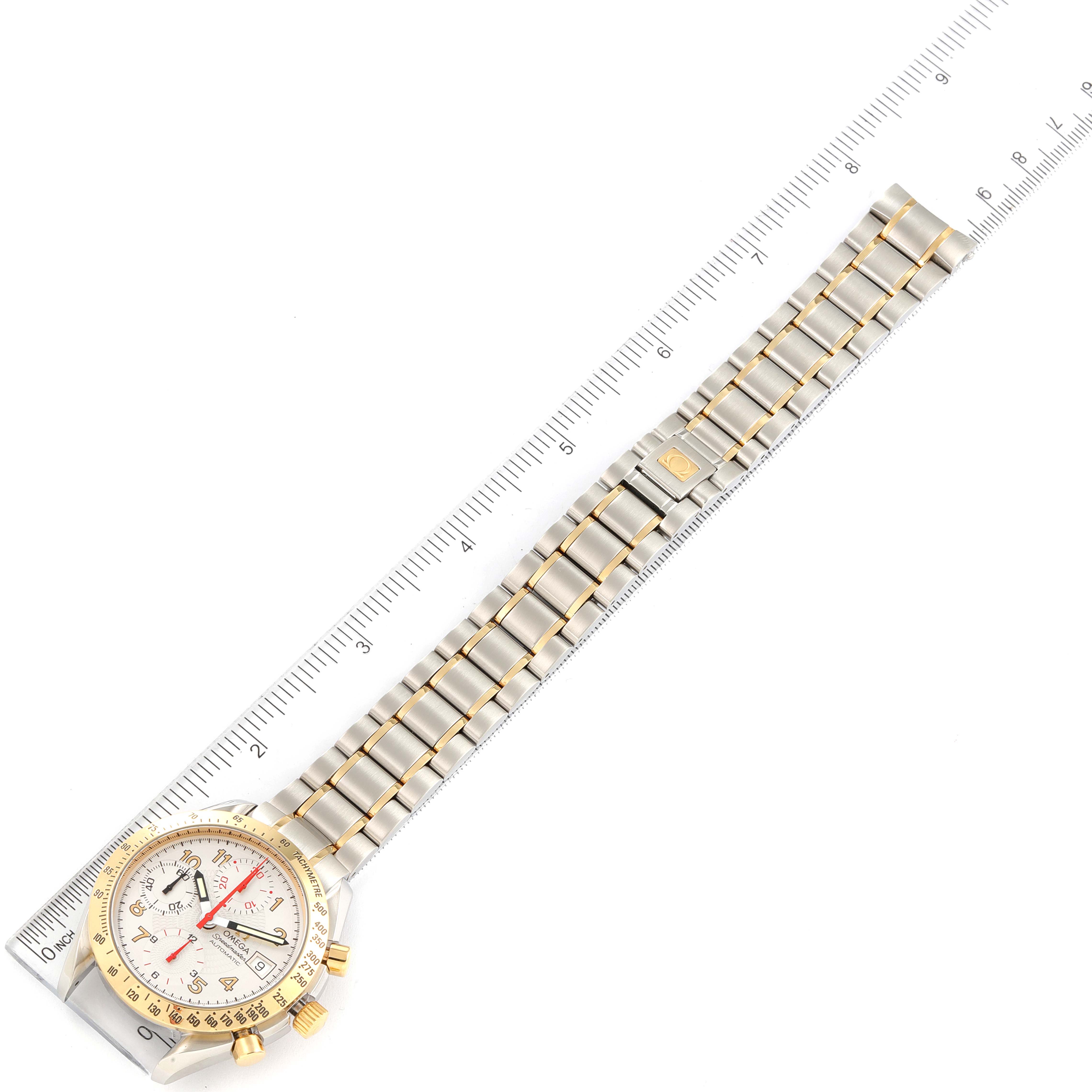 The Omega Speedmaster 3313.33.00 Men's Steel and Gold (two tone) White Dial 3313.33.00 Men's Steel and Gold (two tone) White Dial watch is shown from a top-down angle, displaying the entire face and bracelet alongside a ruler for scale.