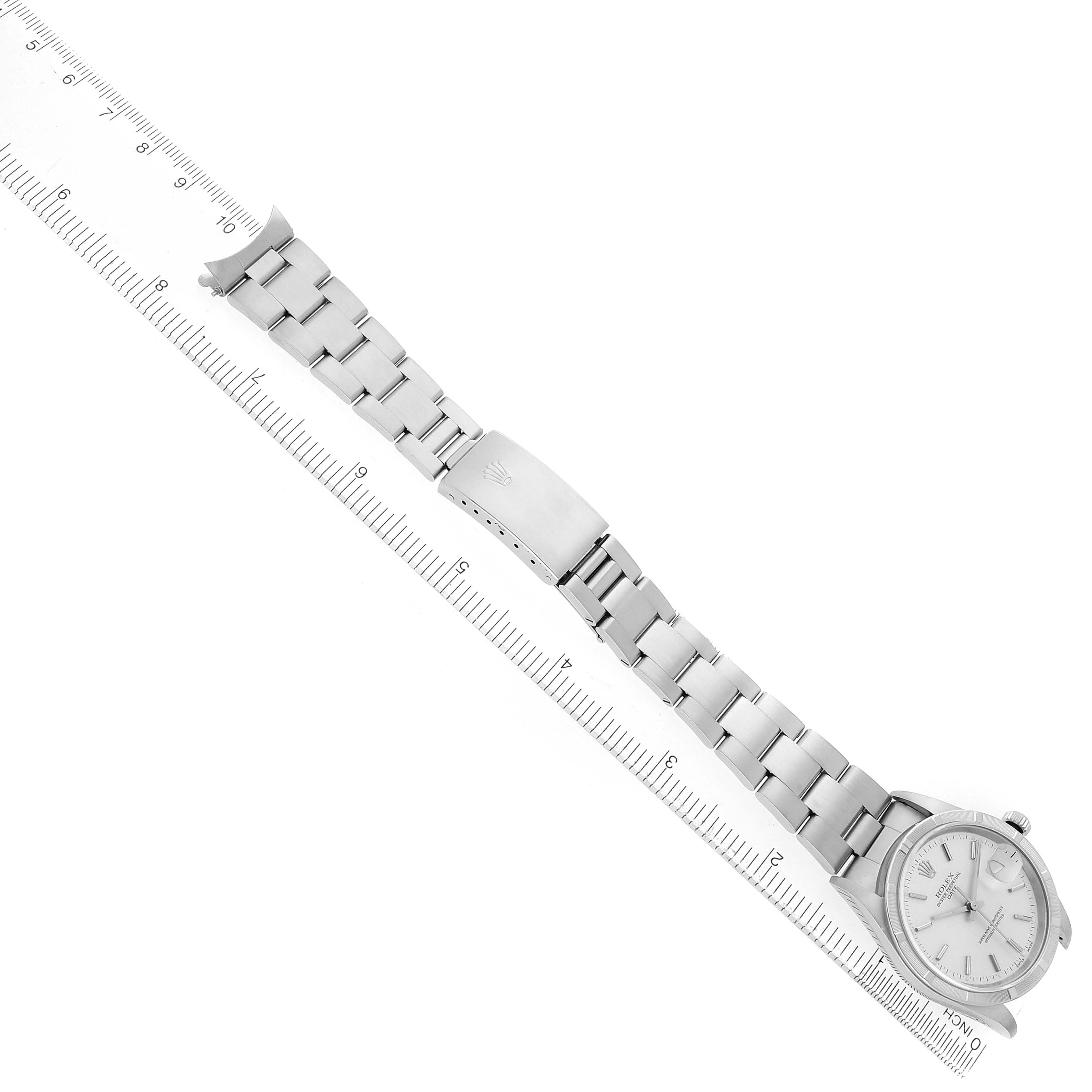 The image shows a Rolex Date 15210 Men's Stainless Steel Silver Dial model watch laid flat, featuring its bracelet, clasp, and dial, next to a ruler for scale.