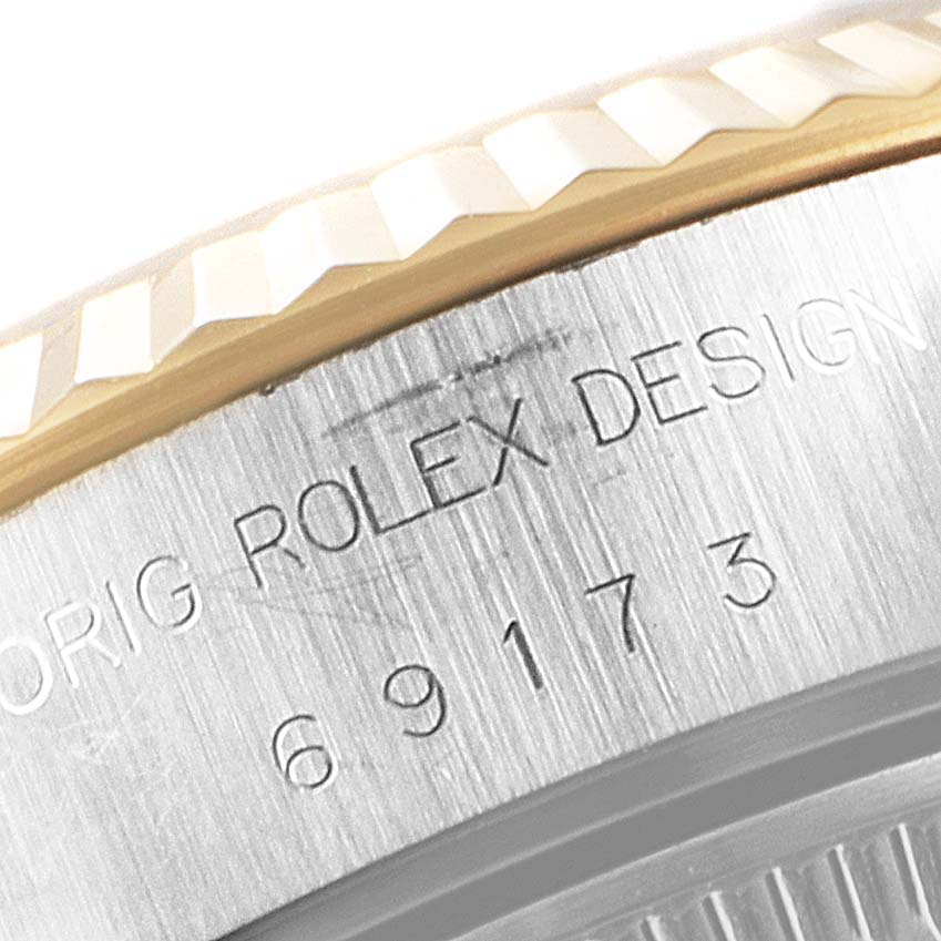 The image shows a close-up of the bezel and case of a Rolex Datejust 69173 Women
s Steel and Gold (two tone) Champagne Dial 69173 Women
s Steel and Gold (two tone) Champagne Dial watch with "Rolex Design" engraving.