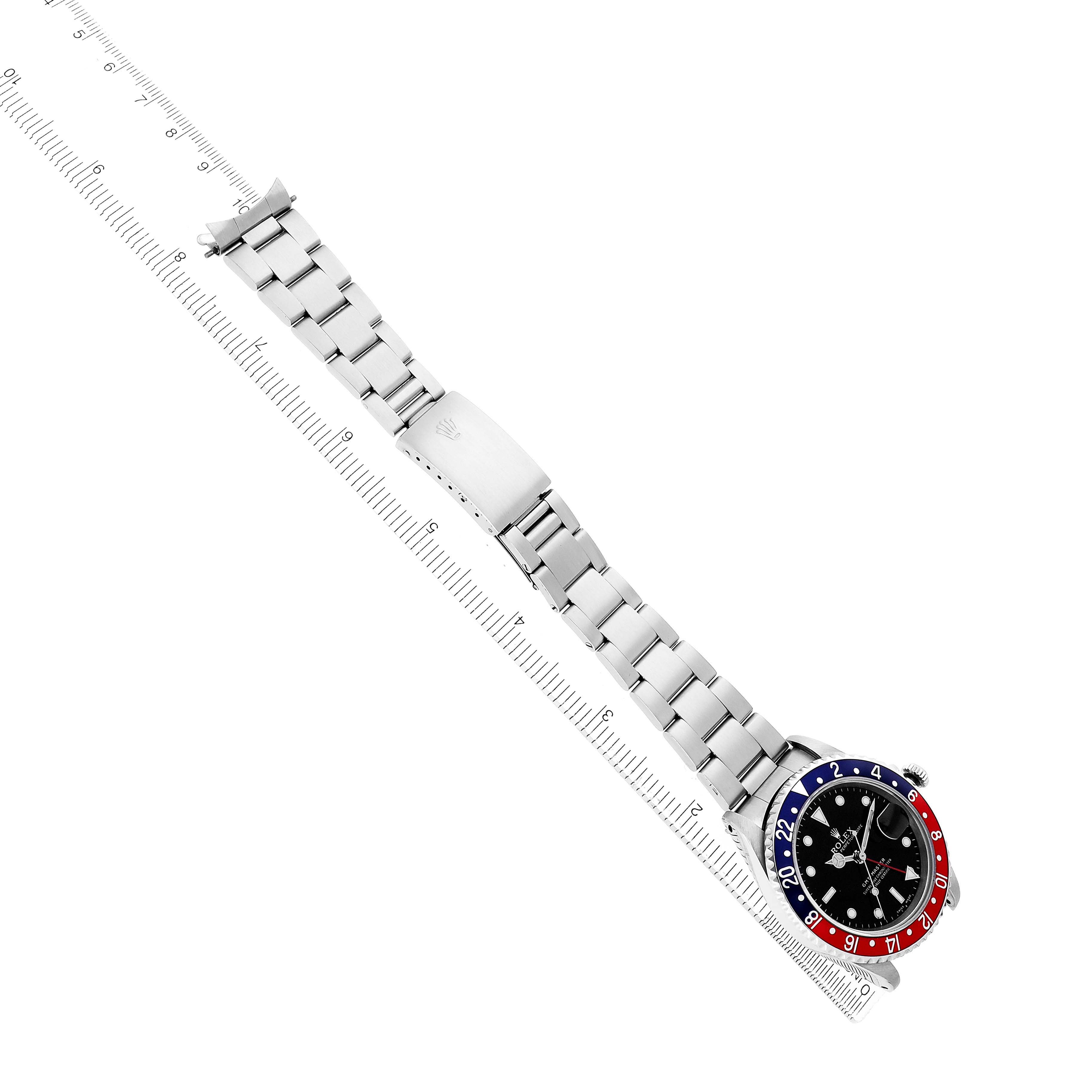 The Rolex GMT-Master 16700 Men's Stainless Steel Black Dial watch is shown from a top view, displaying the bracelet, clasp, and bezel on a ruler.