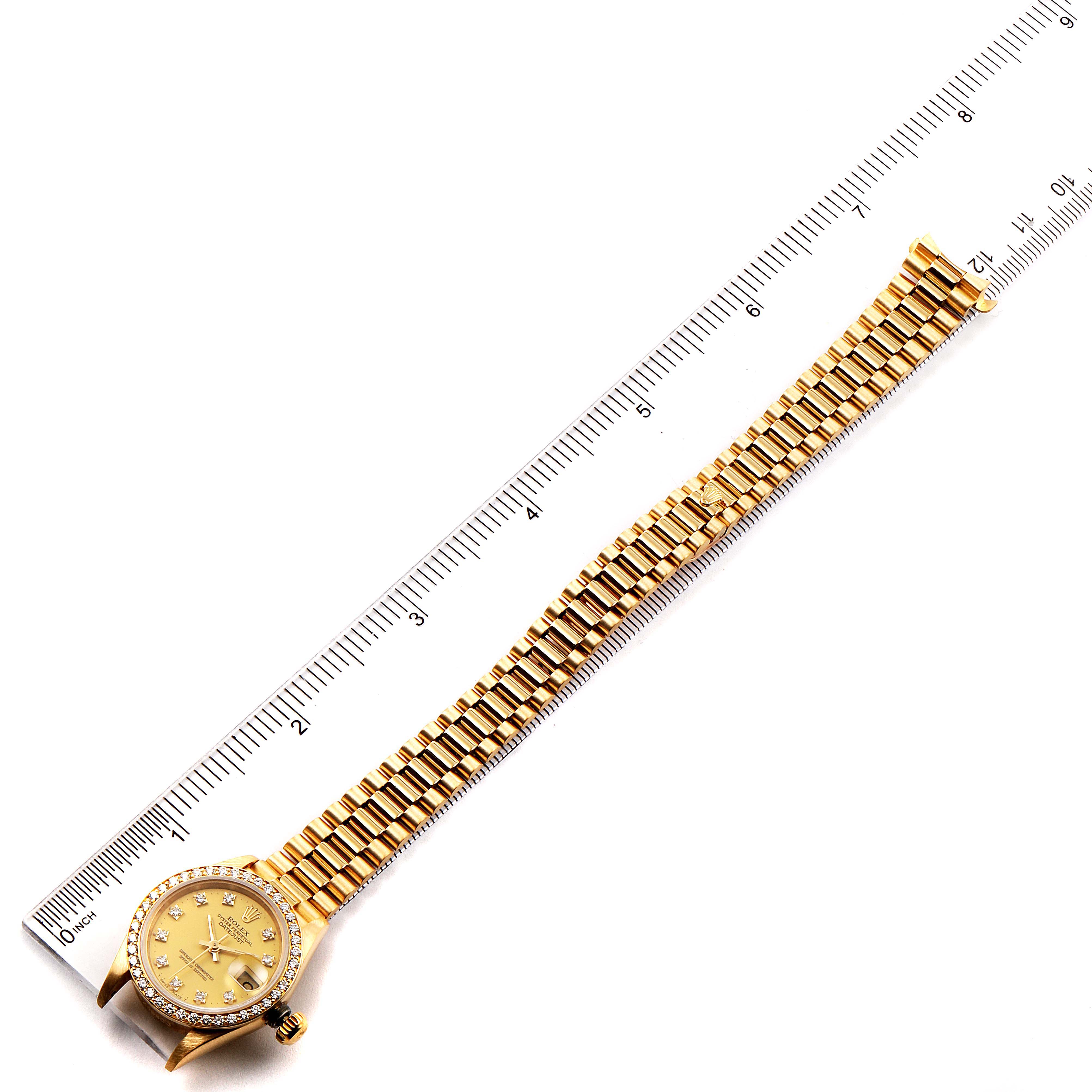 This image shows a Rolex President 69138 Women
s Yellow Gold Champagne Dial 69138 Women
s Yellow Gold Champagne Dial model watch laid flat next to a ruler, highlighting its length and details.