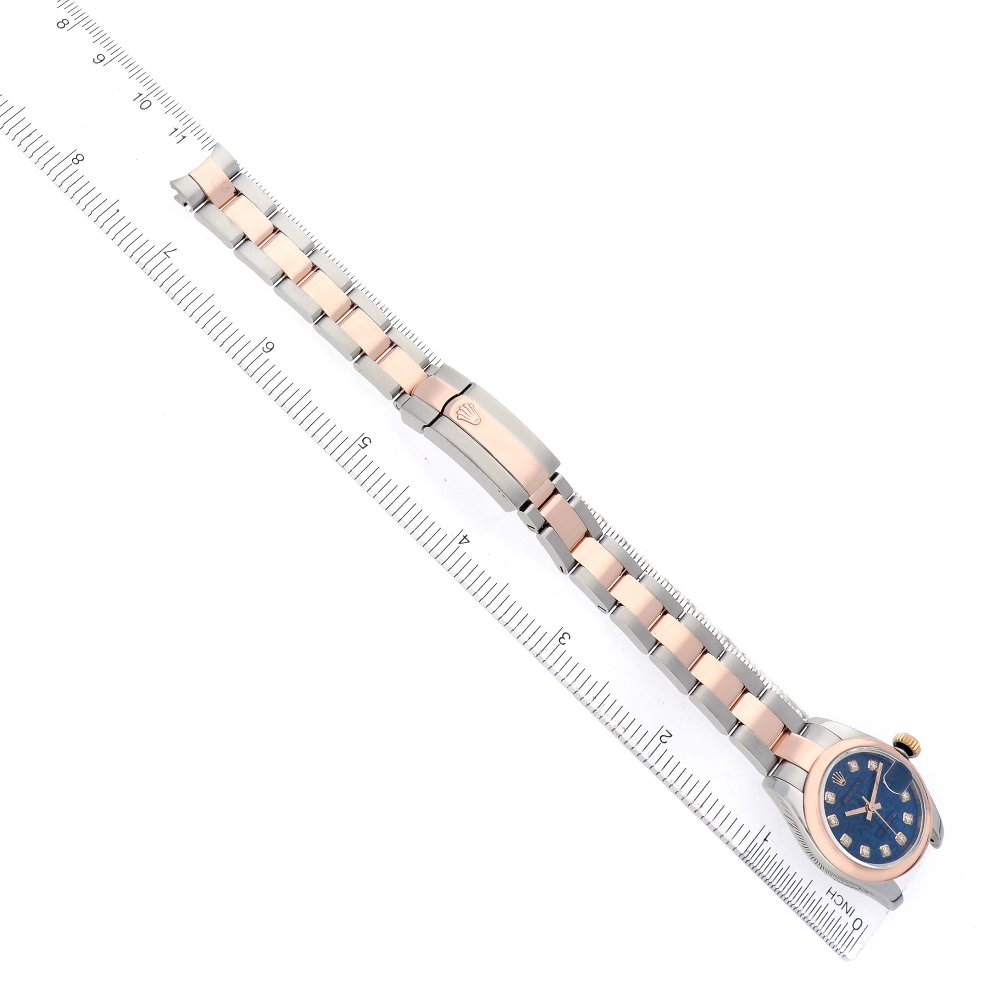 The Rolex Datejust 179161 Women's Rose Gold Blue Dial watch is shown from a top-down angle, displaying the face, bracelet, and clasp along a ruler.