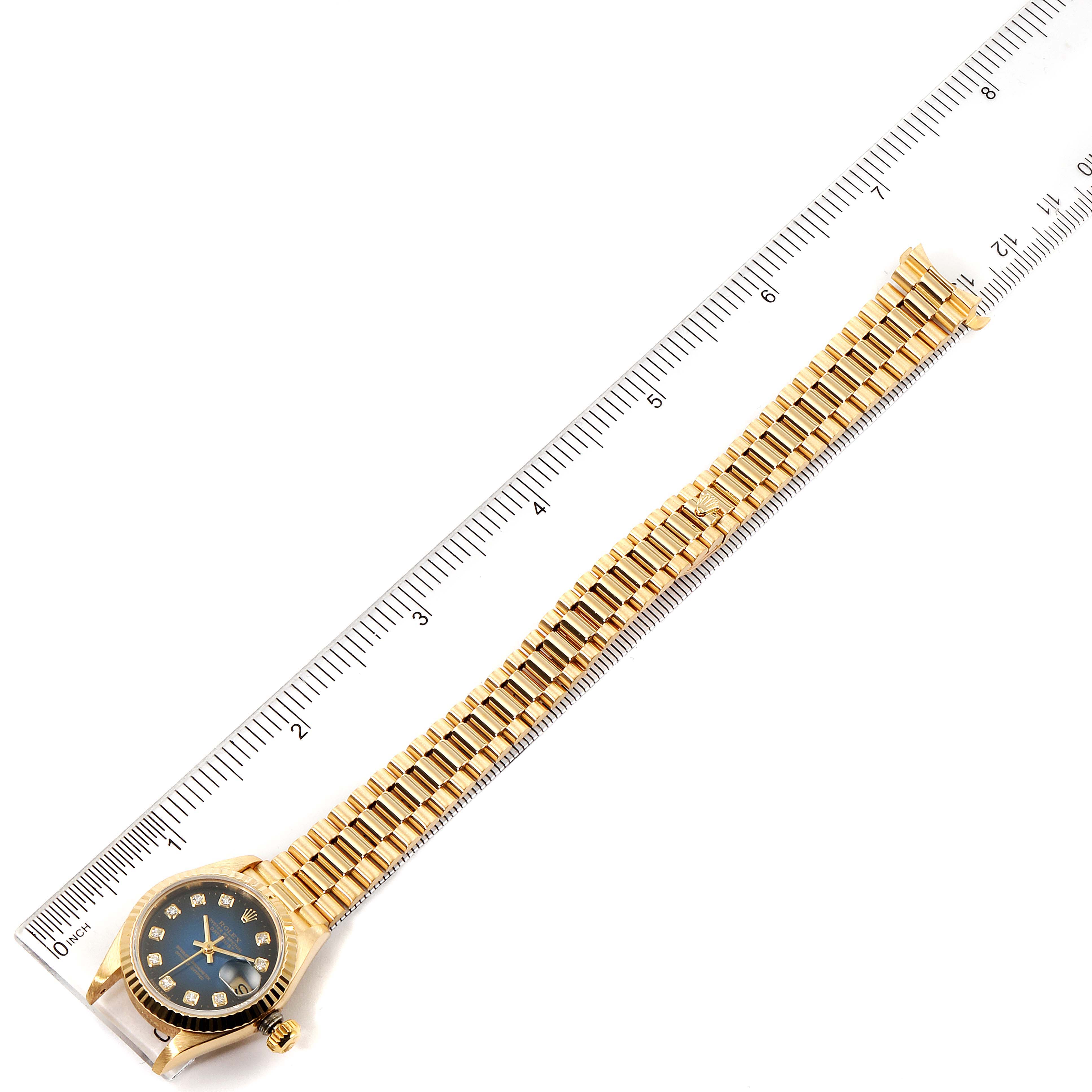 The image shows an aerial view of the Rolex President 69178 Women's Yellow Gold Blue Dial 69178 Women's Yellow Gold Blue Dial watch, displaying its band, case, and a part of a ruler for scale.