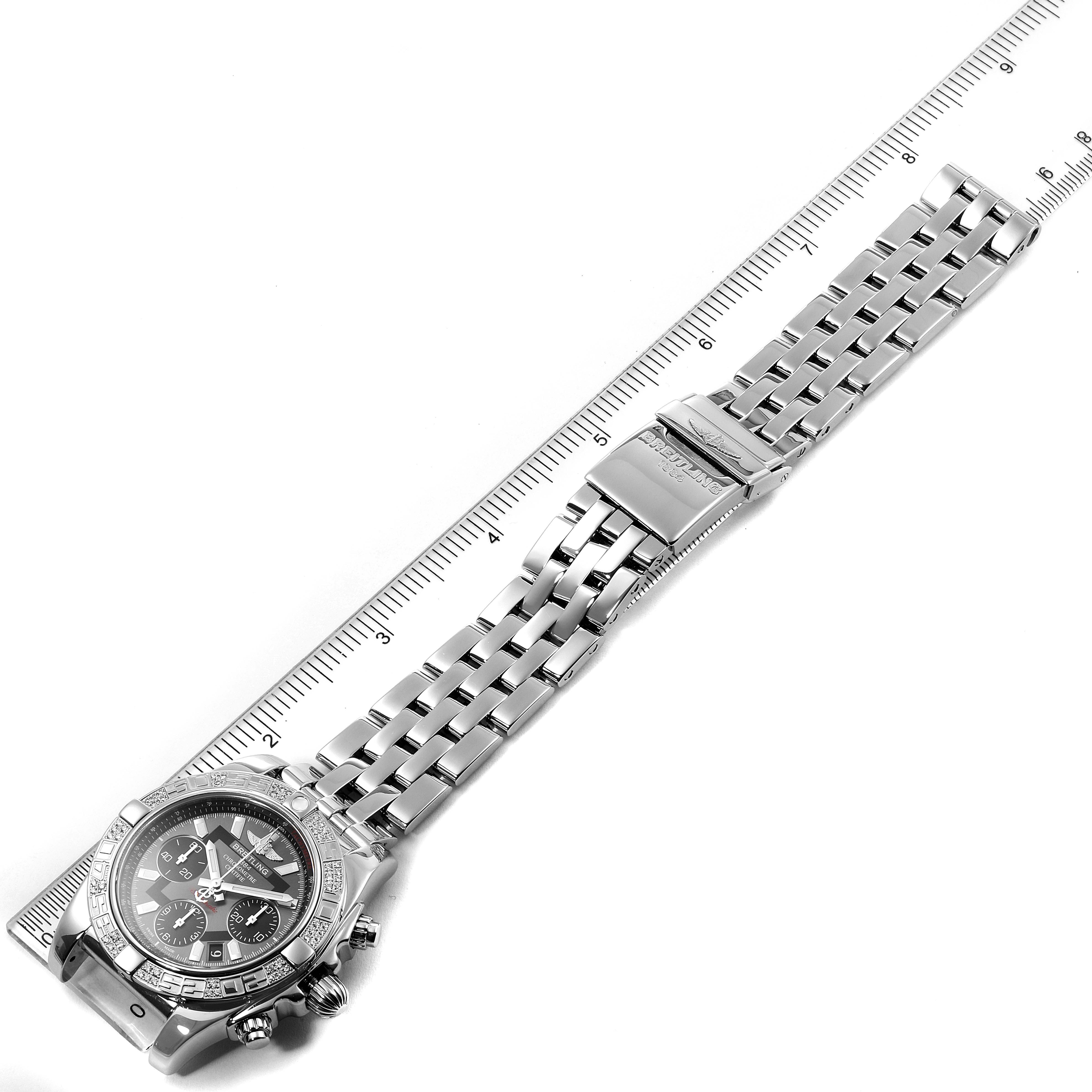 The Breitling Chronomat AB0140 Men's Stainless Steel Grey Dial AB0140 Men's Stainless Steel Grey Dial watch is shown diagonally, featuring its face, bezel, pushers, and metal bracelet with a clasp, lying beside a ruler.