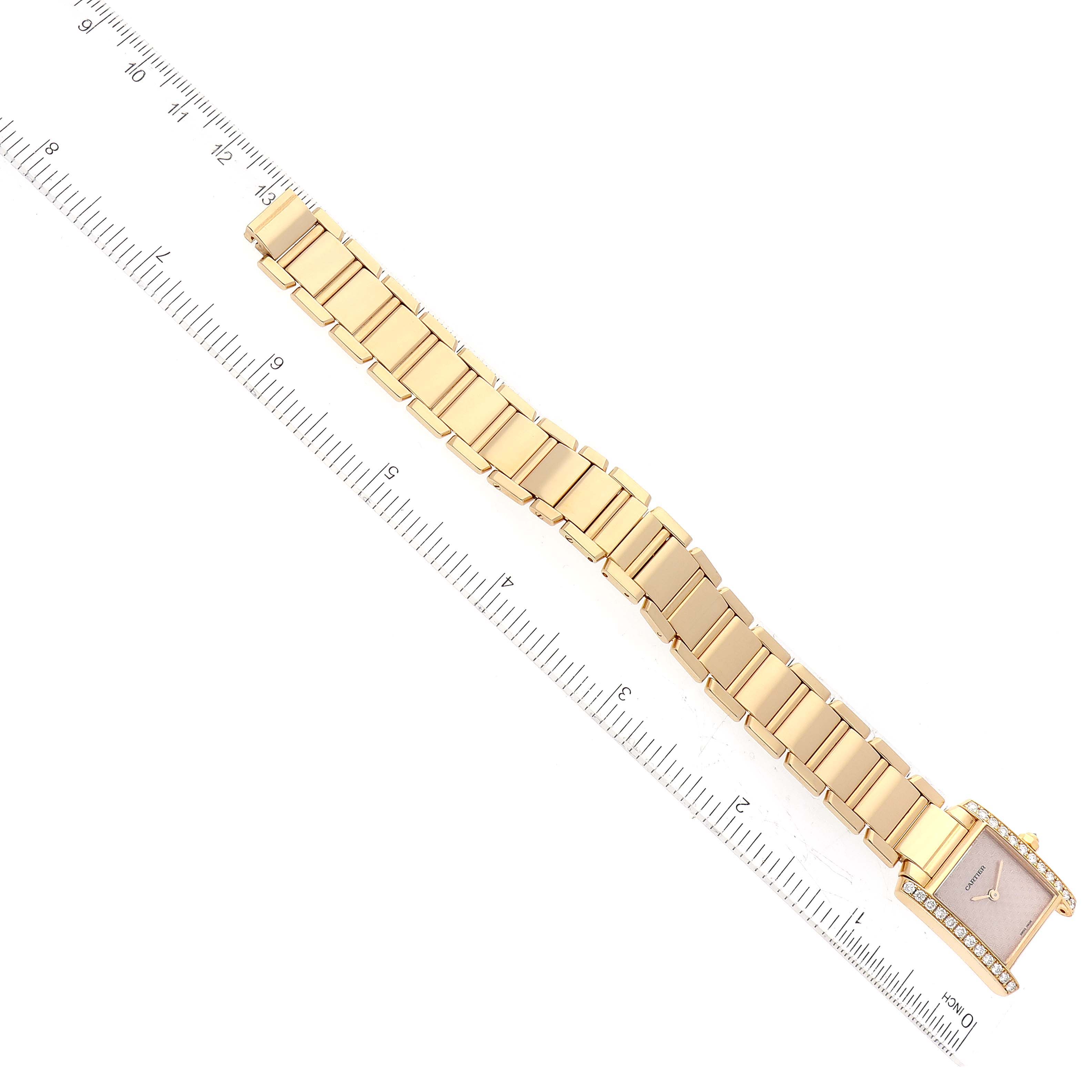 This is an overhead view of the Cartier Tank Francaise WE1021R8 Women's Yellow Gold Pink Dial WE1021R8 Women's Yellow Gold Pink Dial watch with its gold link bracelet and a ruler for scale.