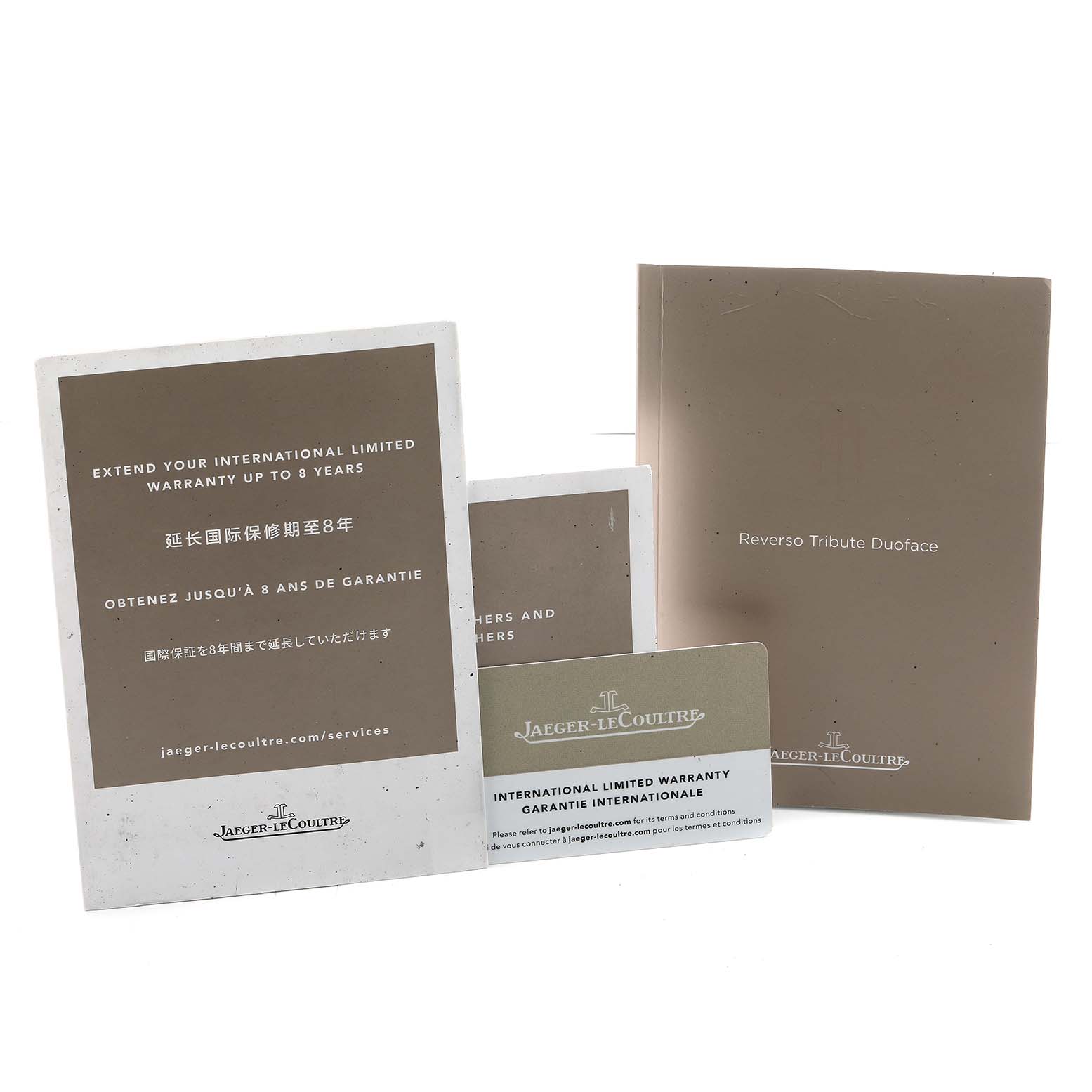 The image shows documentation and warranty cards for the Jaeger-LeCoultre Reverso model, displayed from a front angle.