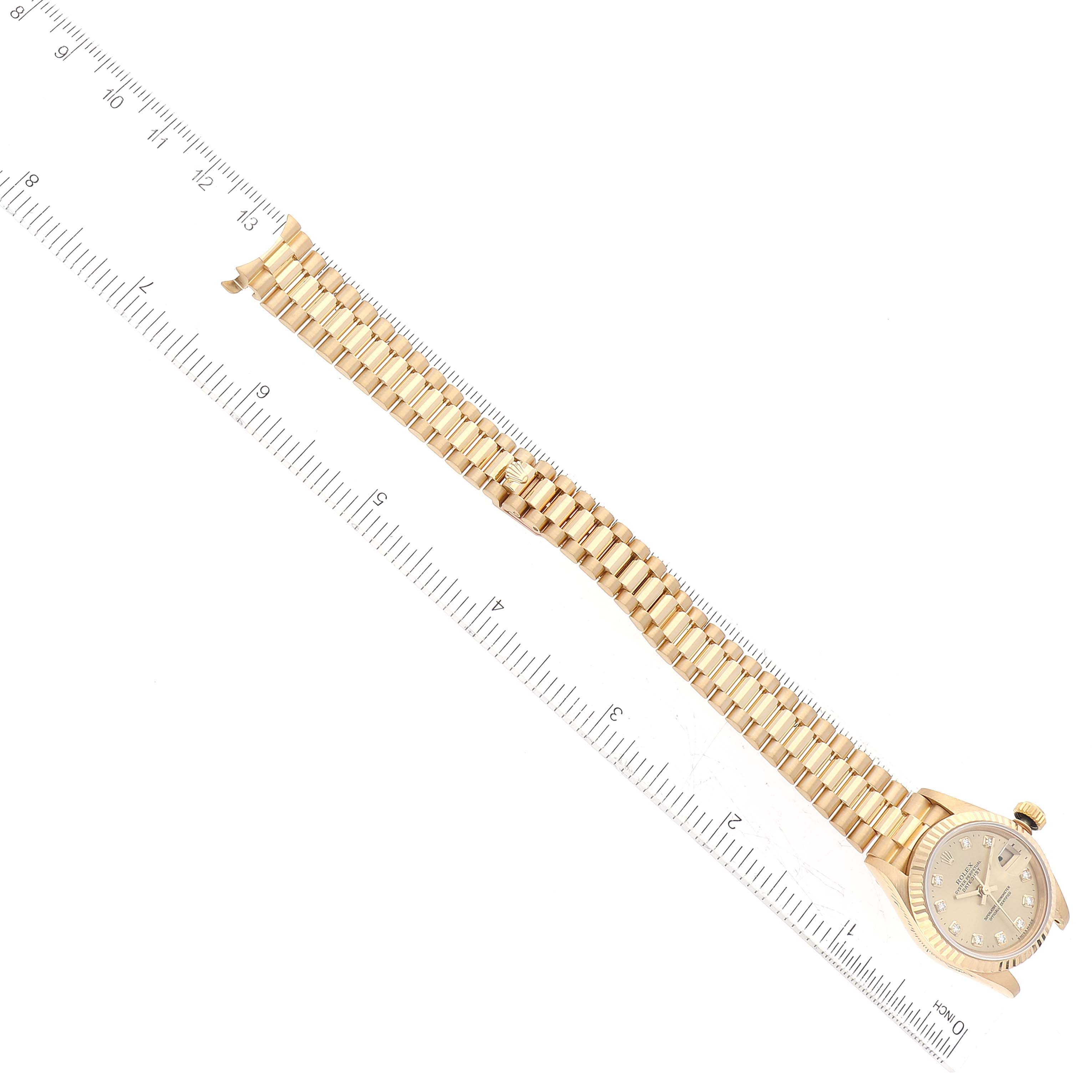 The Rolex President 69178G Women's Yellow Gold Champagne Dial 69178G Women's Yellow Gold Champagne Dial model watch is shown at an angled top view, featuring its dial, case, and full bracelet beside a ruler.